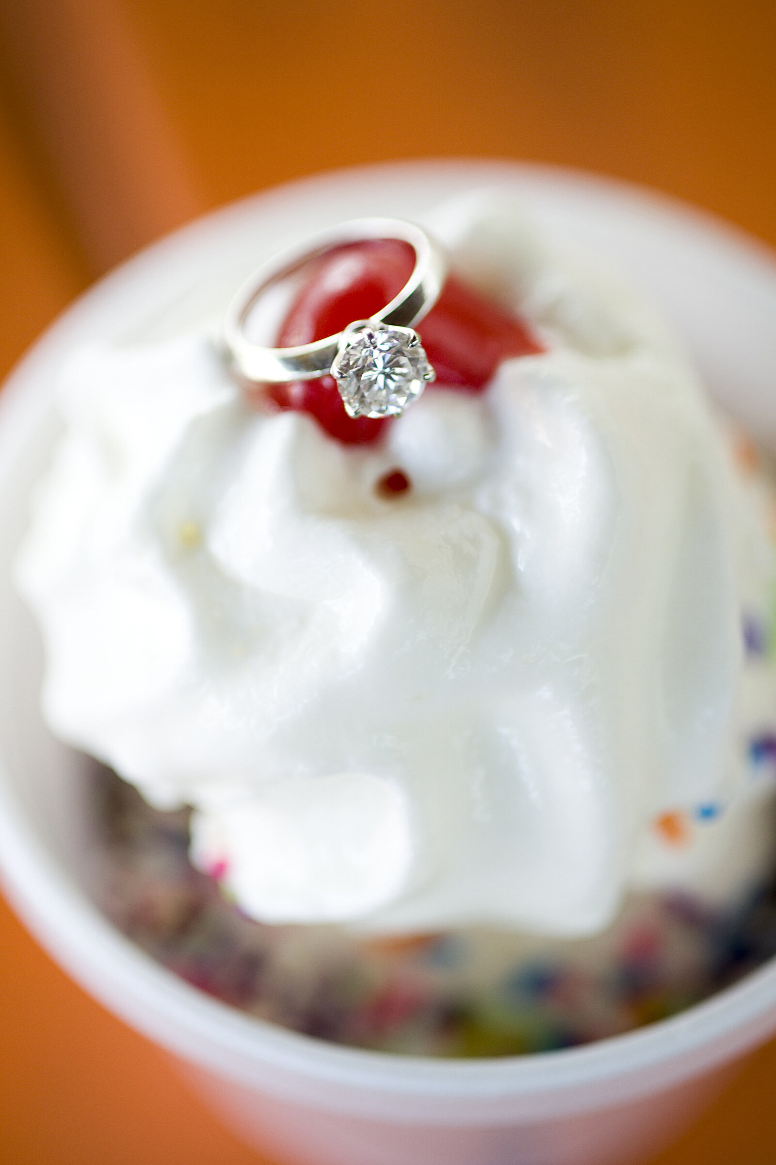 An engagement ring sitting in whipped cream at the top of a sundae 