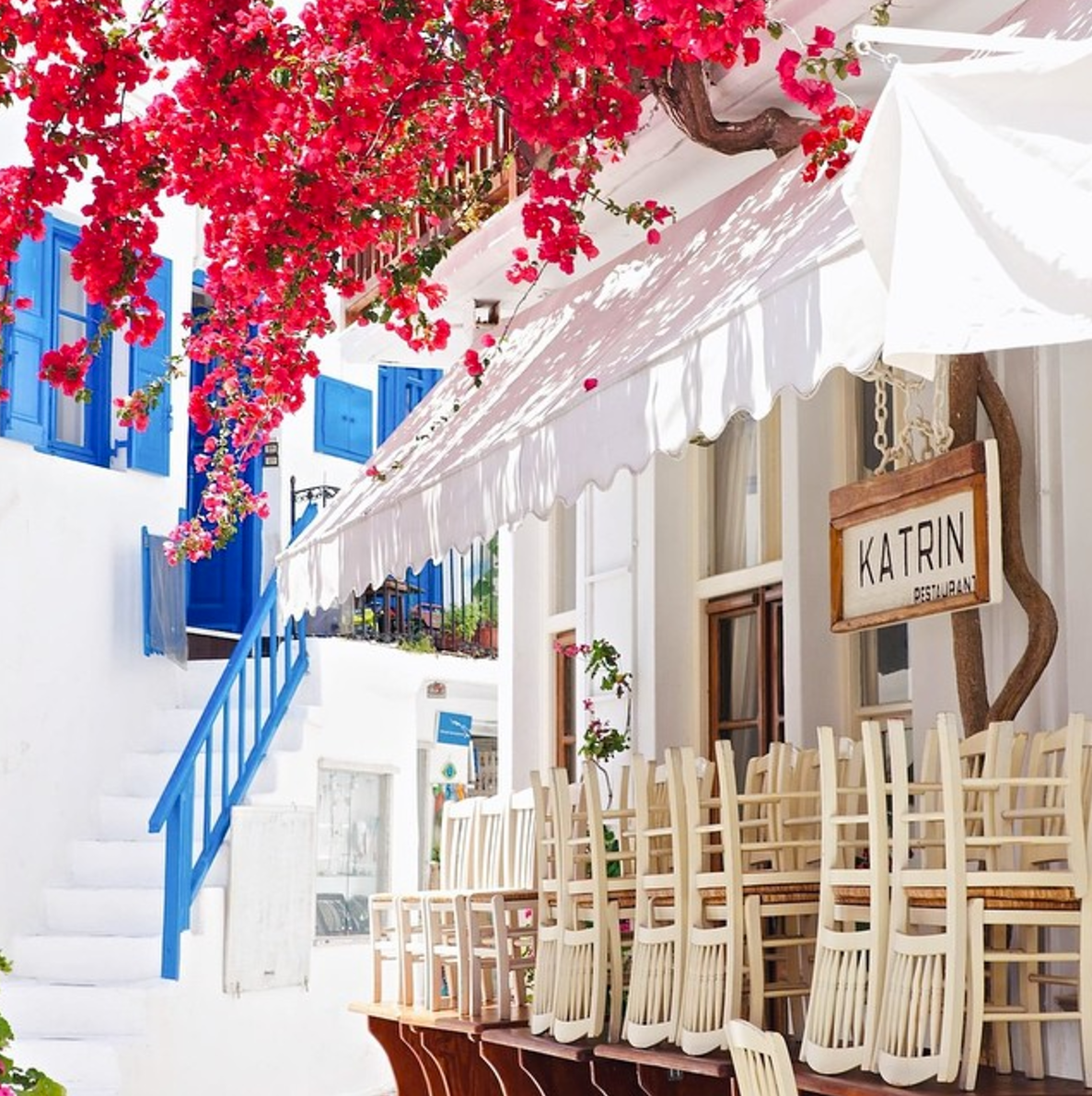 Travel photographer Chelsea Loren in Mykonos Greece restaurant cafe blue white alley with pink flowers