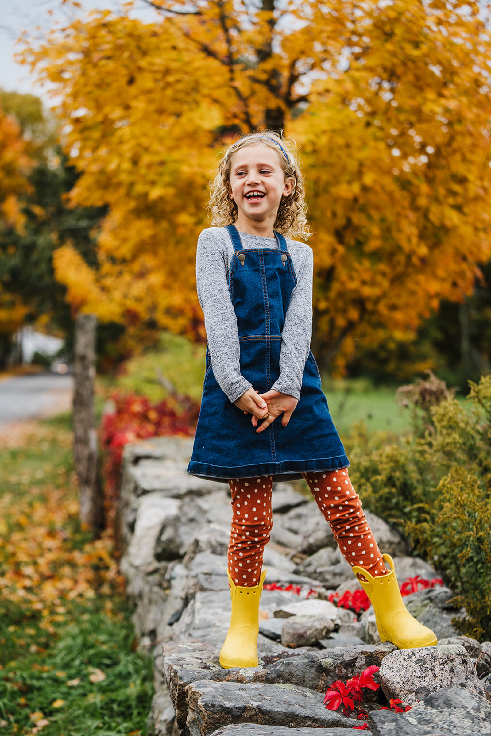 girl in yellow boots stands on rock wall in autumn