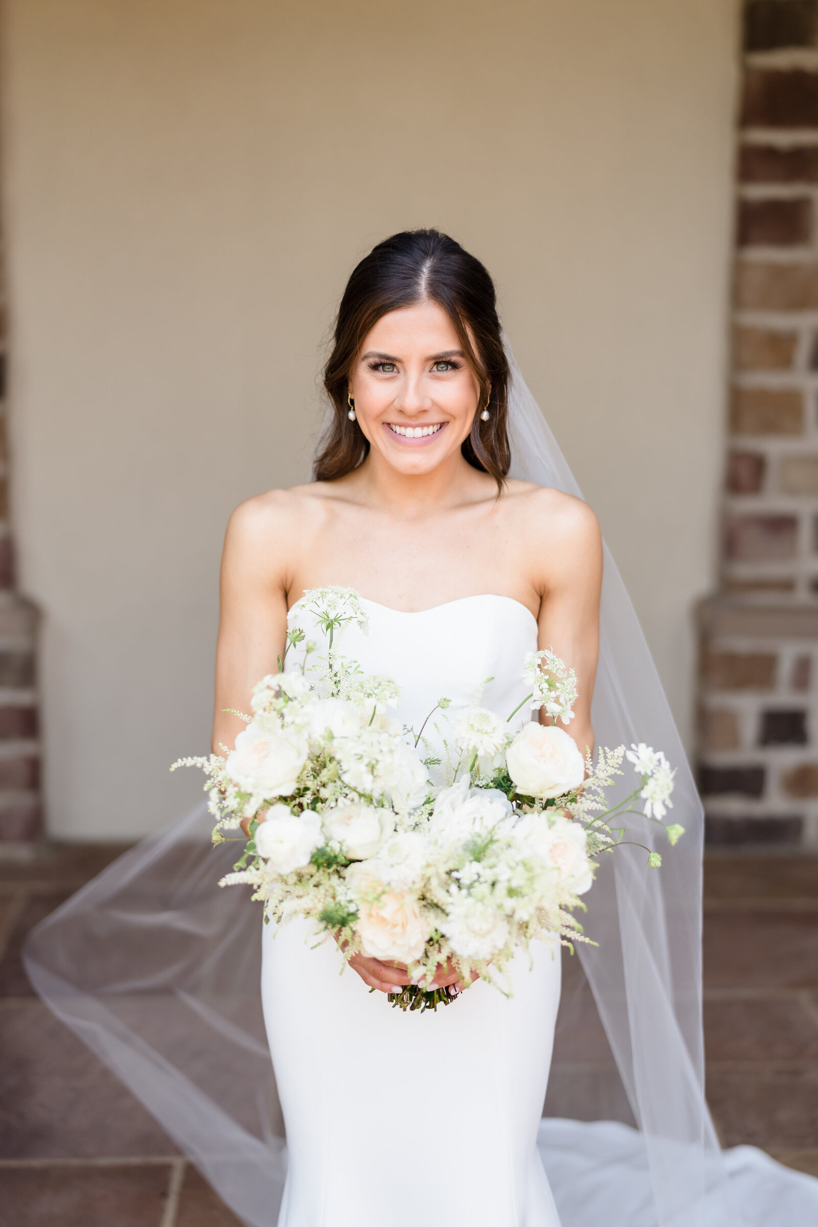 A bride with a large white and groom bouquet smiles outside the ceremony space at Pinnacle Golf Club