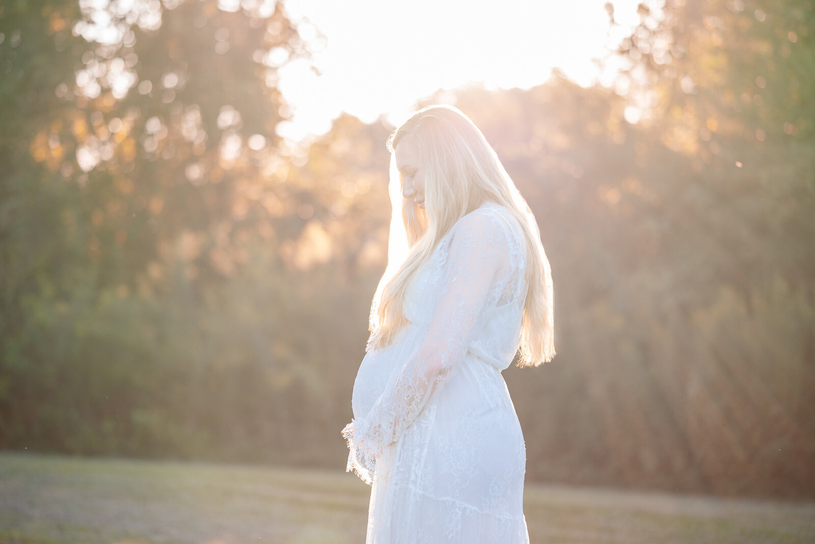 Pregnant mom holding her stomach and looking down at it while the sun sets  behind her  in Huntsville Alabama