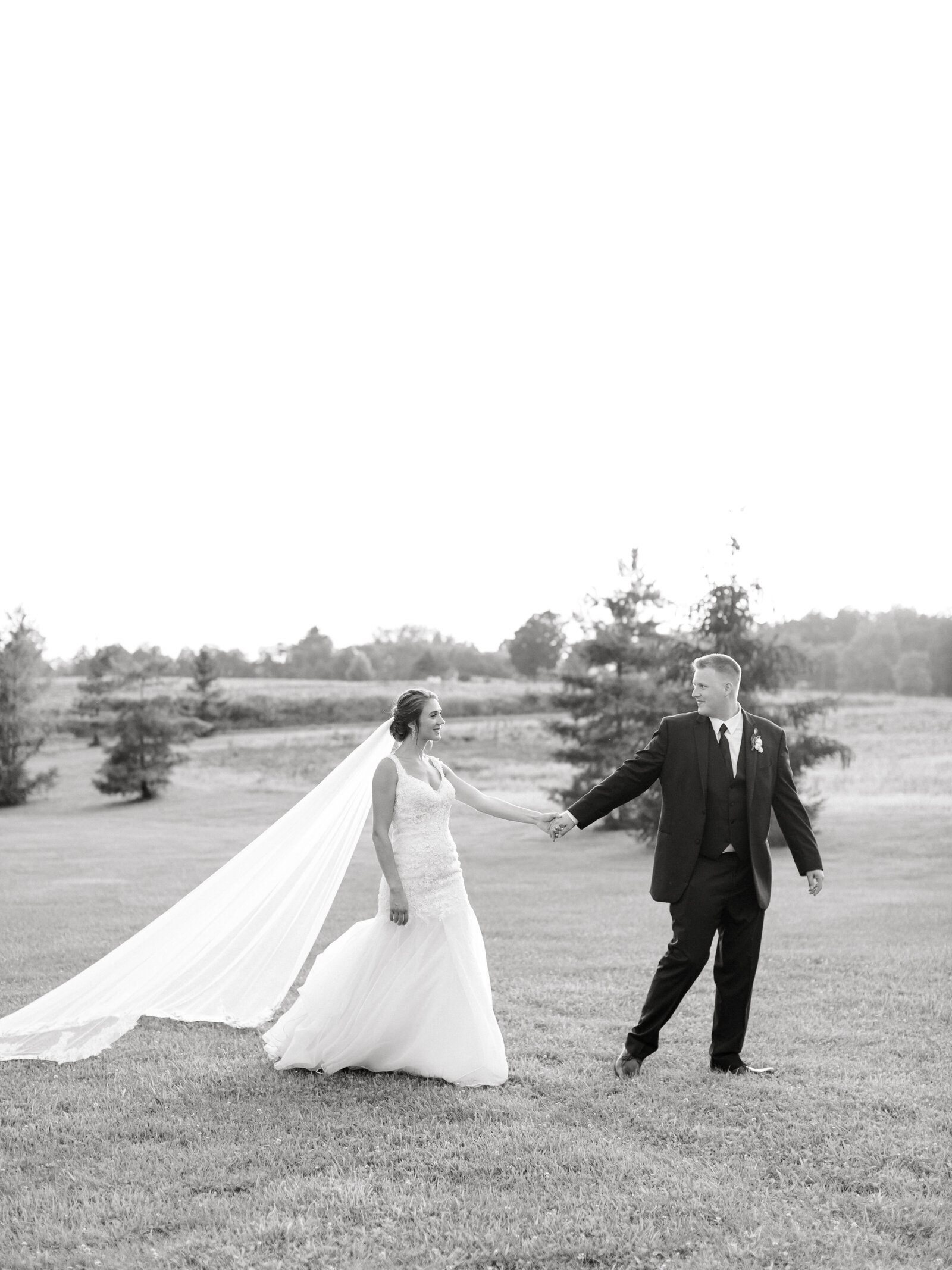 bride ad groom walking holding hands through field at sunset