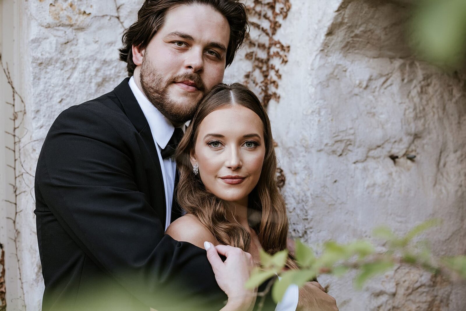 Elegant wedding portrait of a stylish couple embracing against a white stone wall, captured by Houston luxury wedding photographer Logrono & Co.