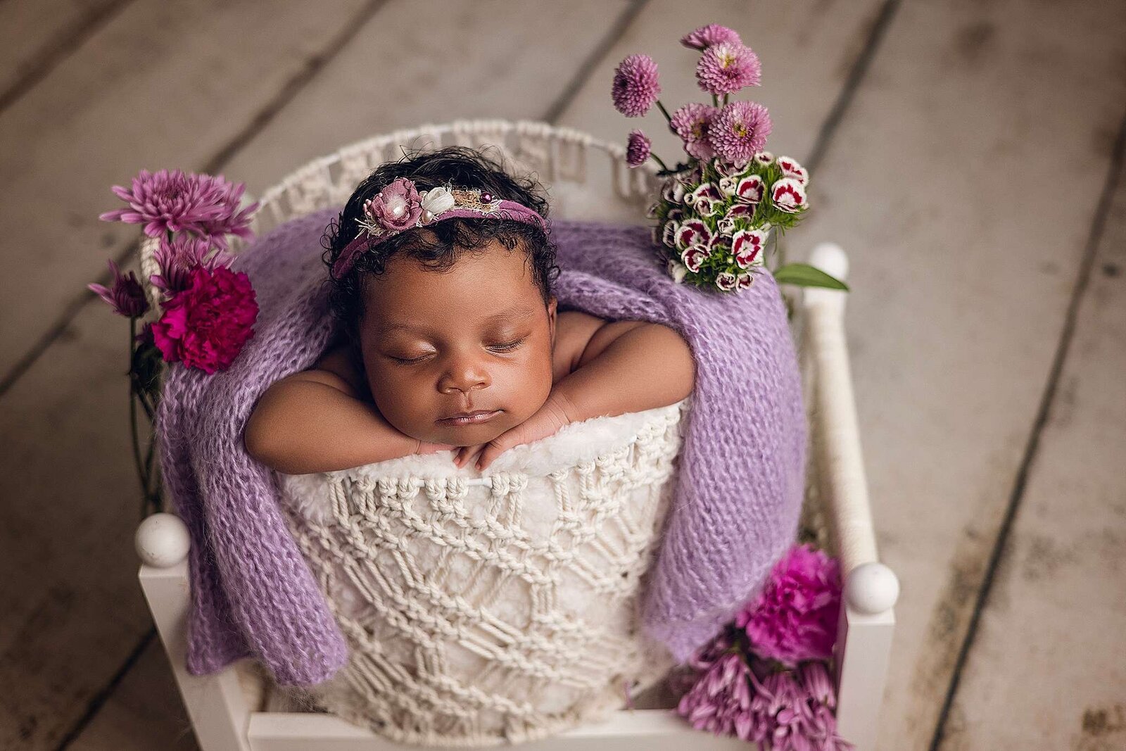  A peaceful baby girl sleeps in a basket surrounded by vibrant purple flowers.