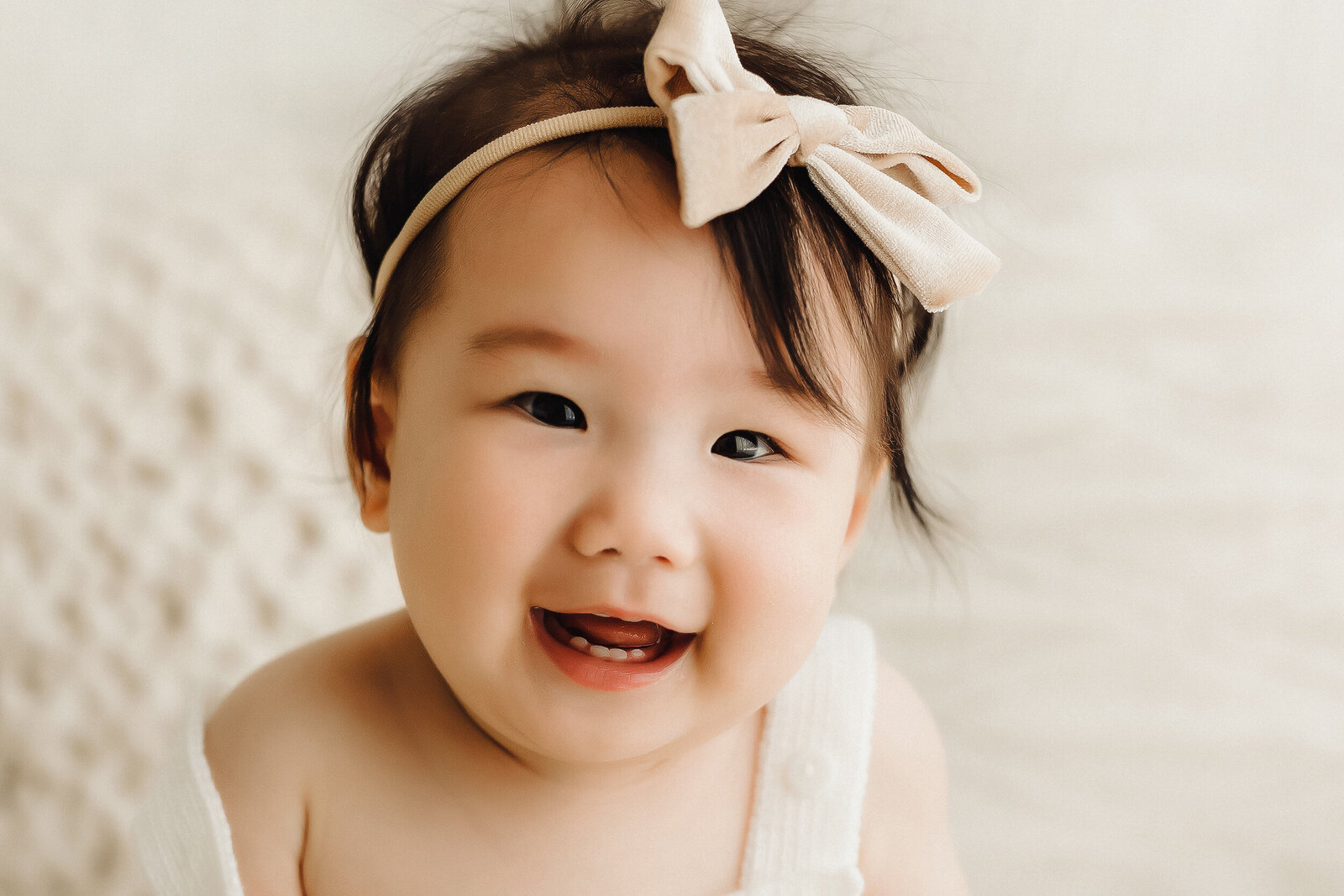A 9 month old baby girl smiles wide for a picture inside a natural light photography studio near Vancouver Washington
