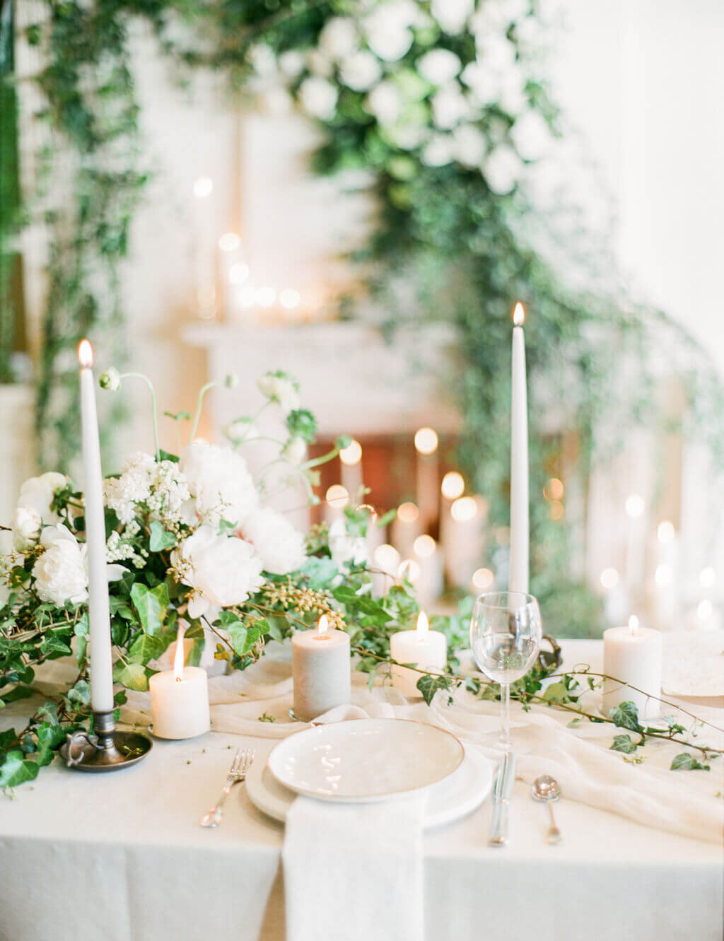 White and beige tablesettings with greenery and candles at fireplace with tall taper candles