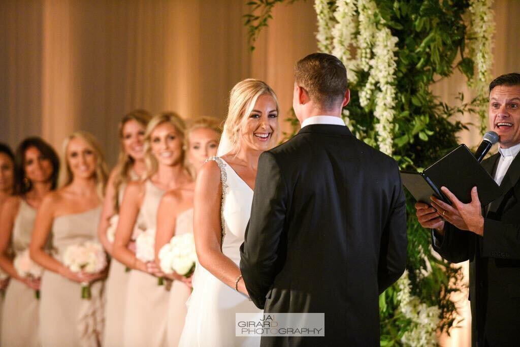 Bride smiles at her groom during wedding ceremony as bridesmaids look on