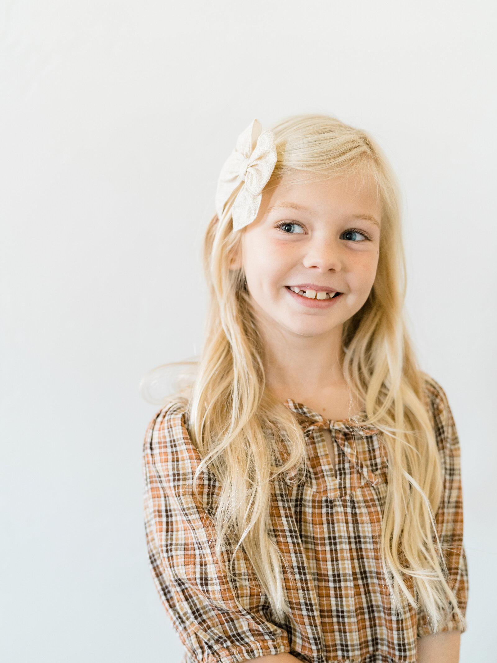 young girl with blonde hair and a plaid dress smiling