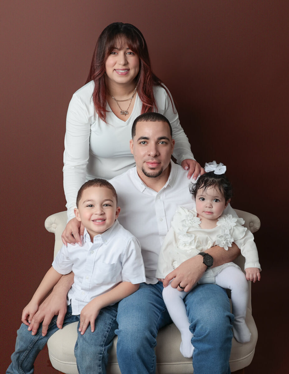 A beautiful family sits on a comfortable couch in a Rochester studio, surrounded by soft lighting, as they engage in a fun photography session to create lasting memories.