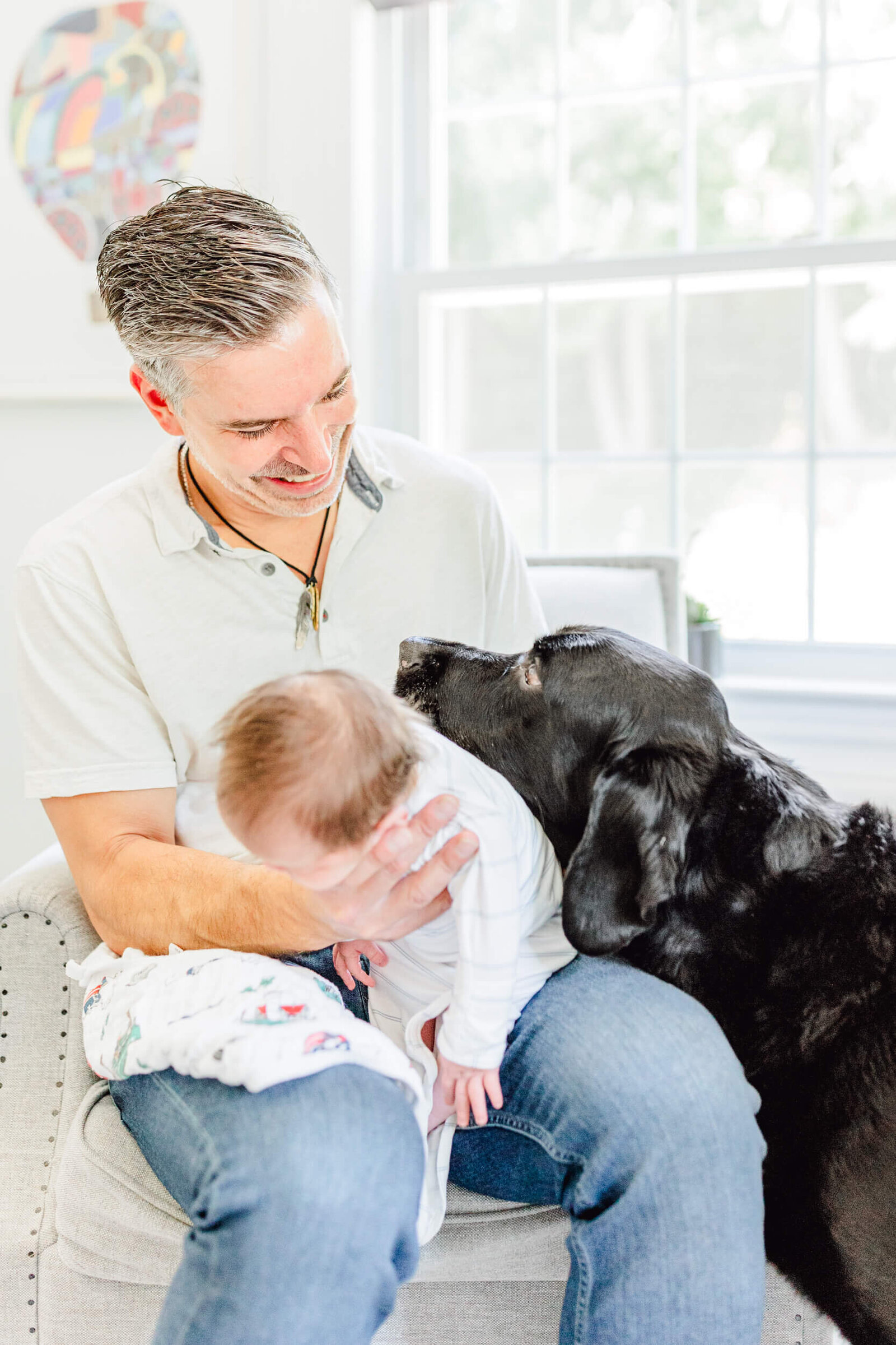 Dad burps his newborn in the nursery and laughs at a curious black lab