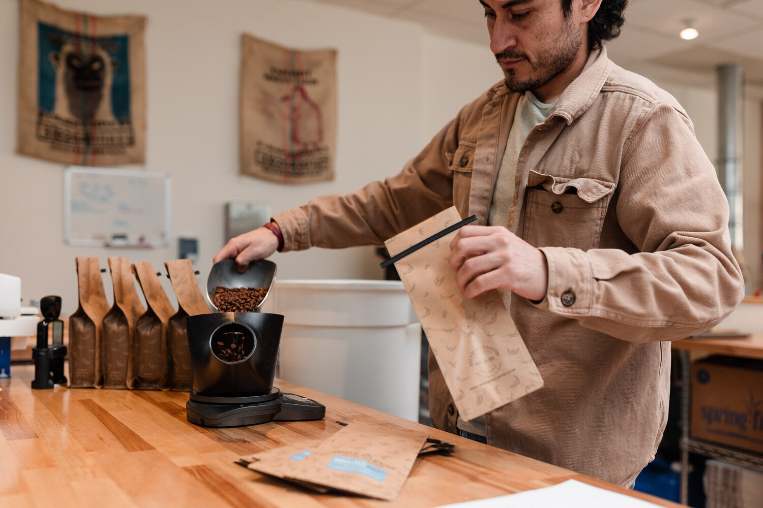 man pouring coffee beans into a small grinder while holding a bag with the other hand