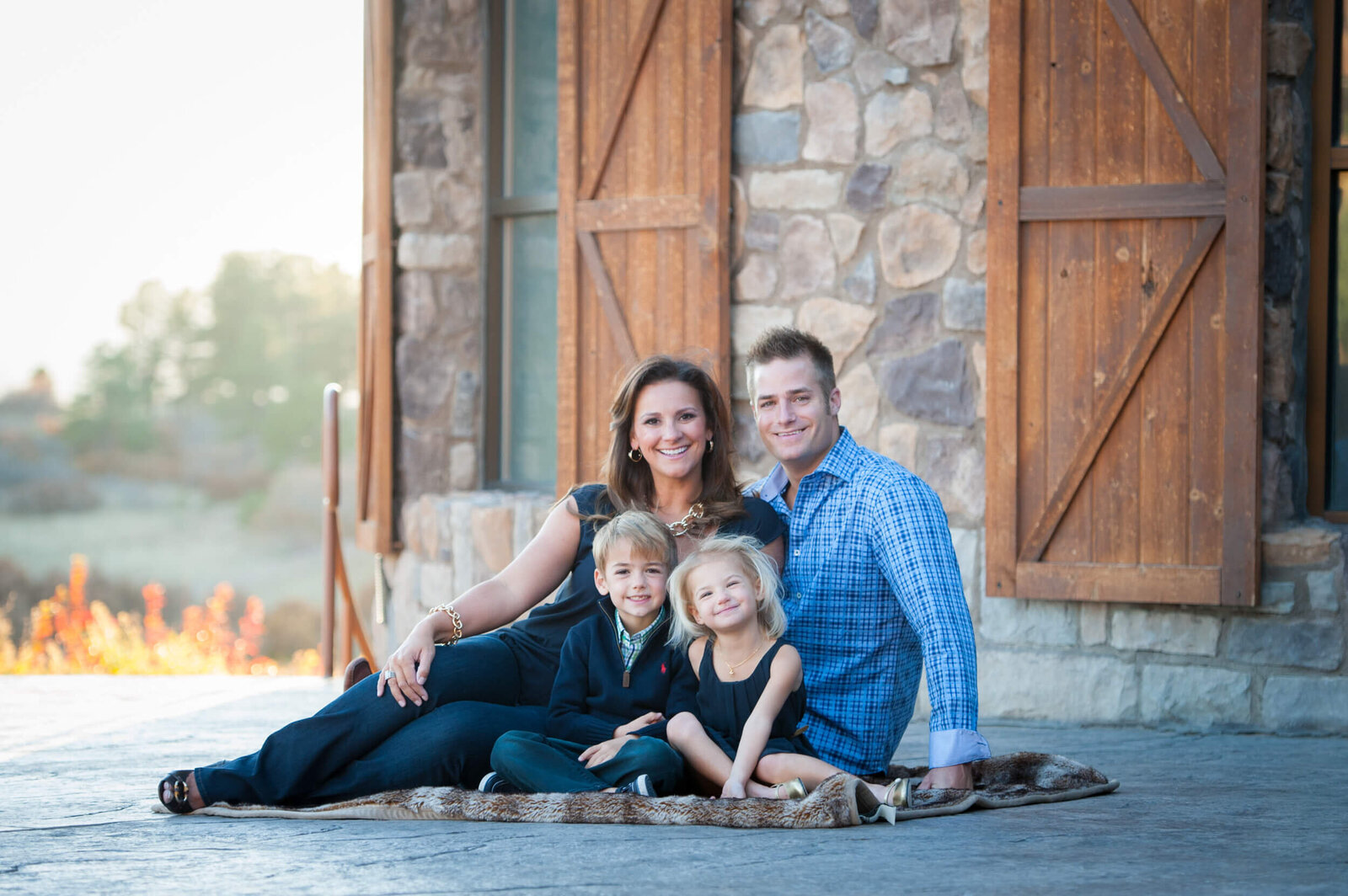 Happy parents sit on a blanket on a stone patio with their toddler son and daughter at sunset