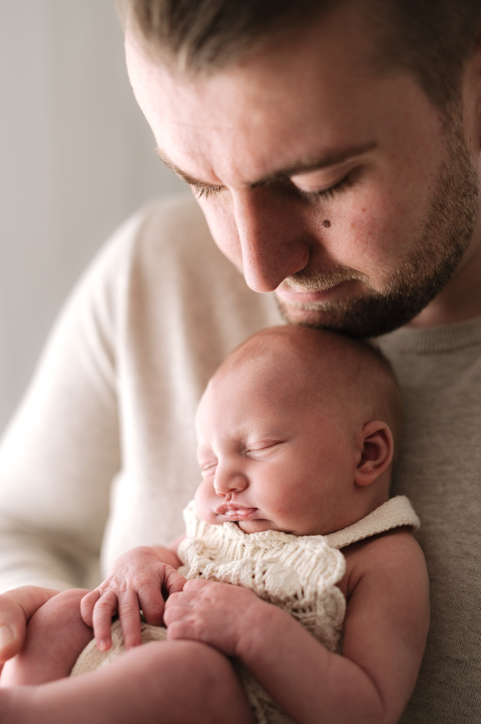 A father holding his newborn daughter under his chin at newborn photoshoot in Billingshurst