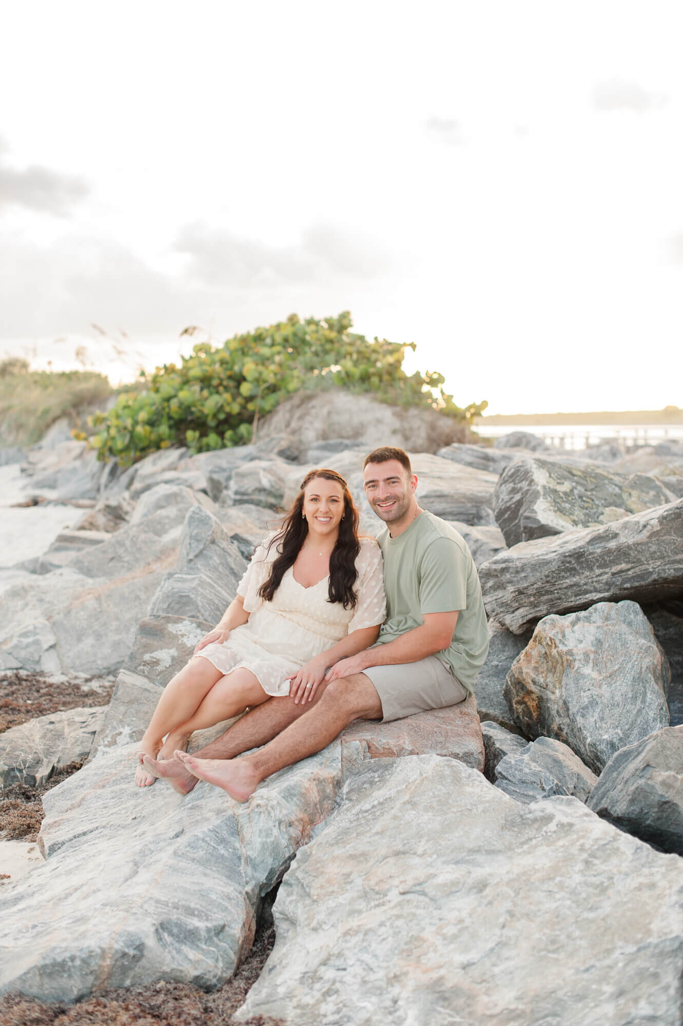 Couple smiles at the camera while sitting on rocks at Jetty Park in Cape Canaveral