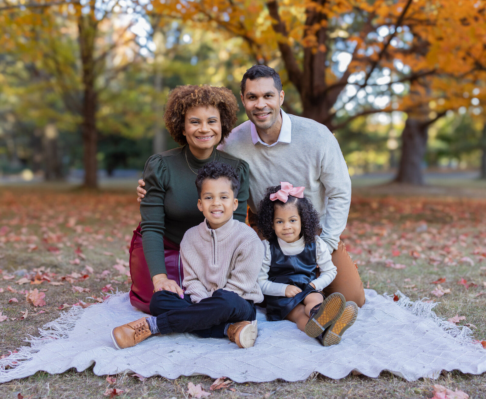 Smiling family of four sitting on blanket during fall photoshoot in Bergen County New Jersey park