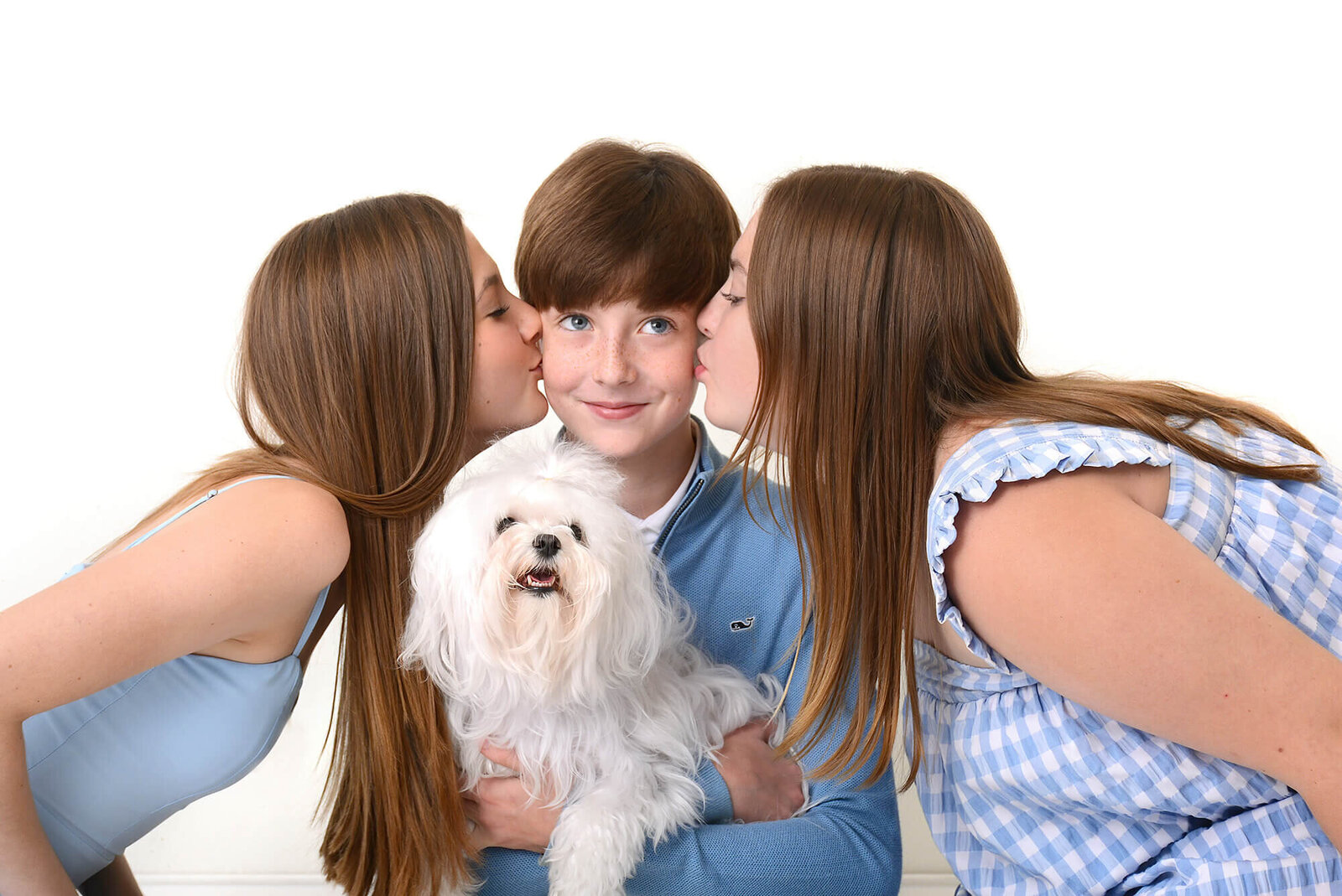 two sisters kiss their brother on the cheek while he holds a adorable puppy