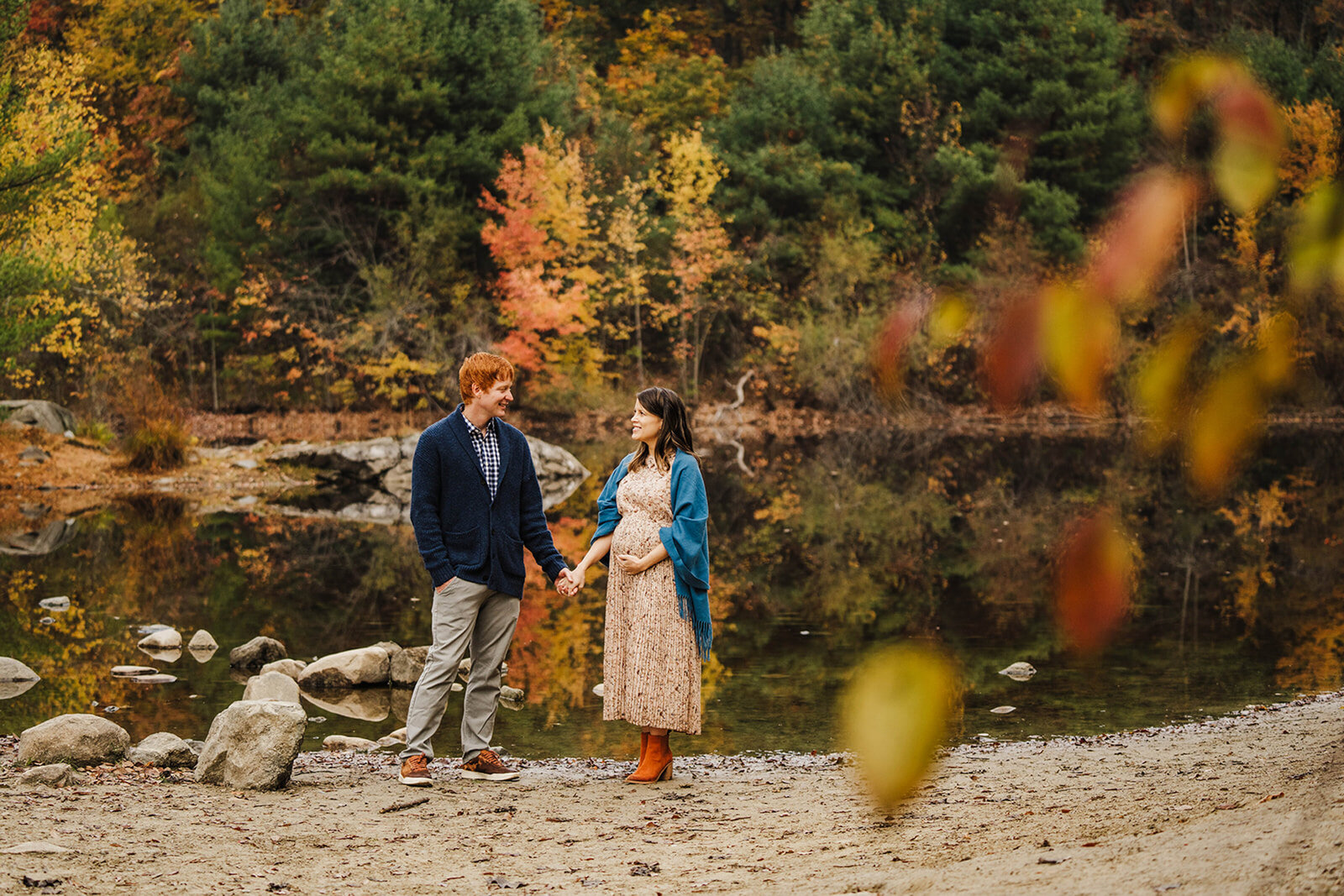 pregnant couple holds hands by lake in autumn