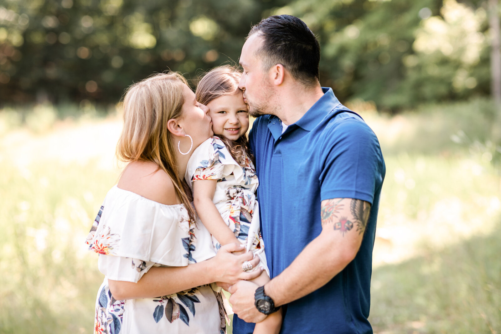 mom and dad kissing daughter for family photos in park