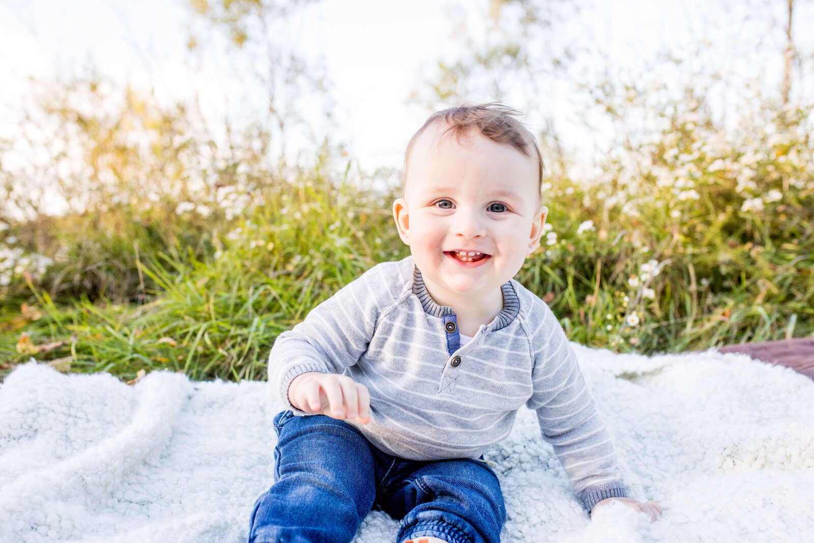Young boy smiling while sitting on blanket in field during family photo session.