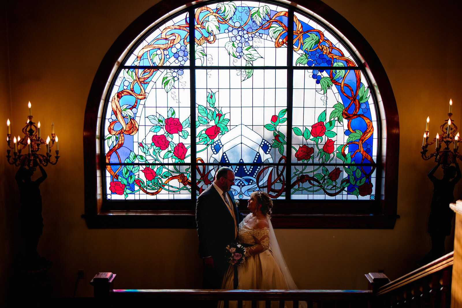 Bride and groom stand for a portrait in front of a beautiful stained glass window