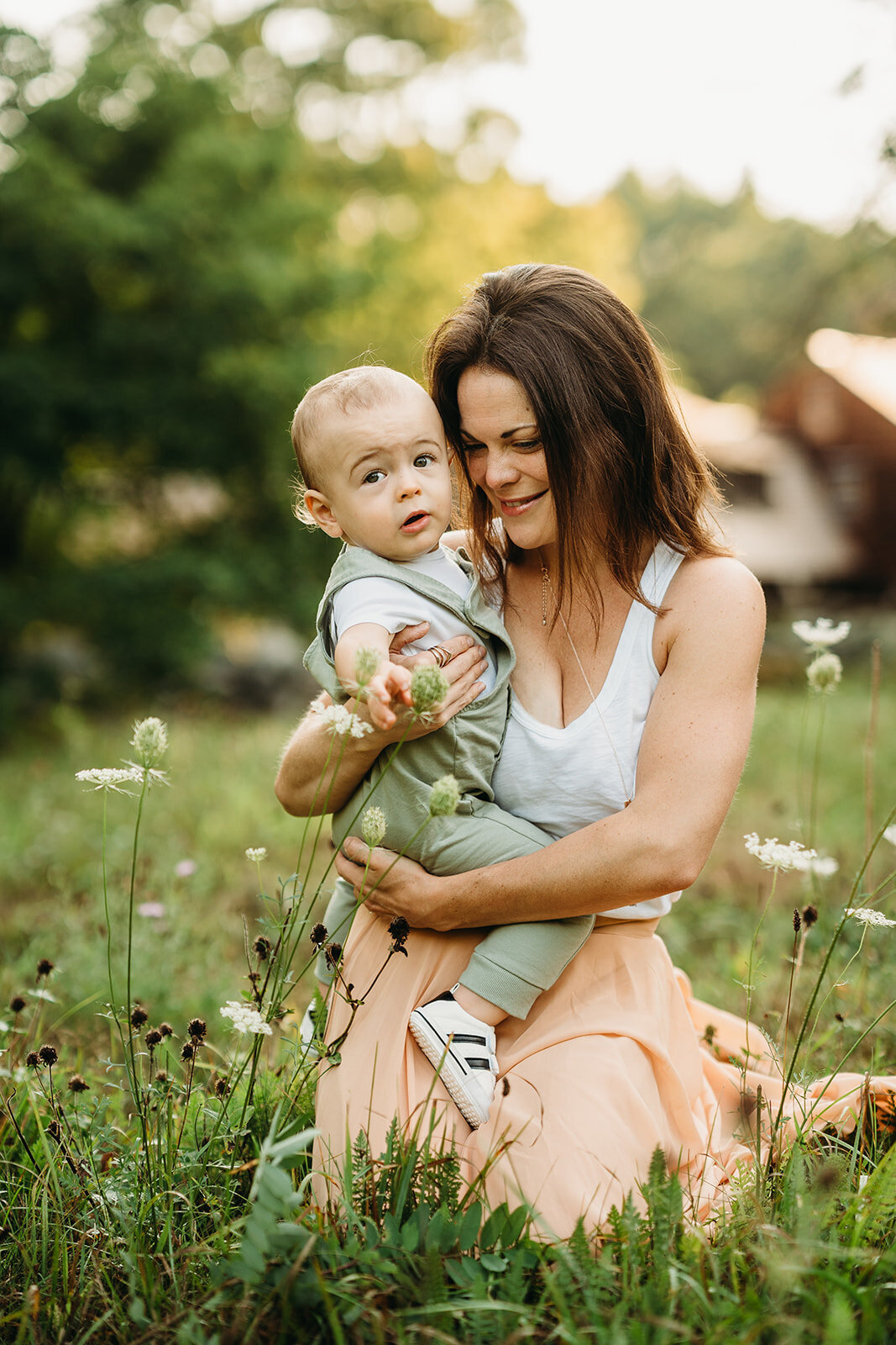 mother in pink skirt holds baby boy in field of flowers