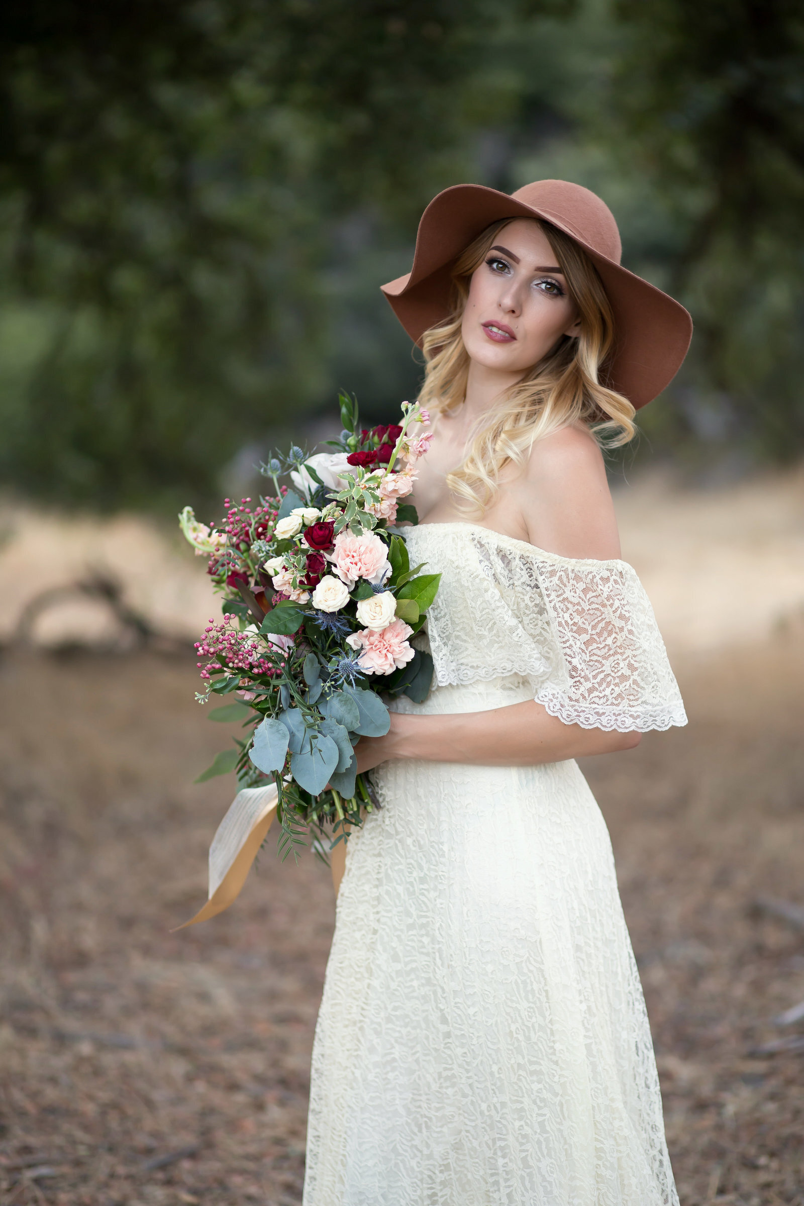 Woman wearing white lace dress and hat holding blush florals outside