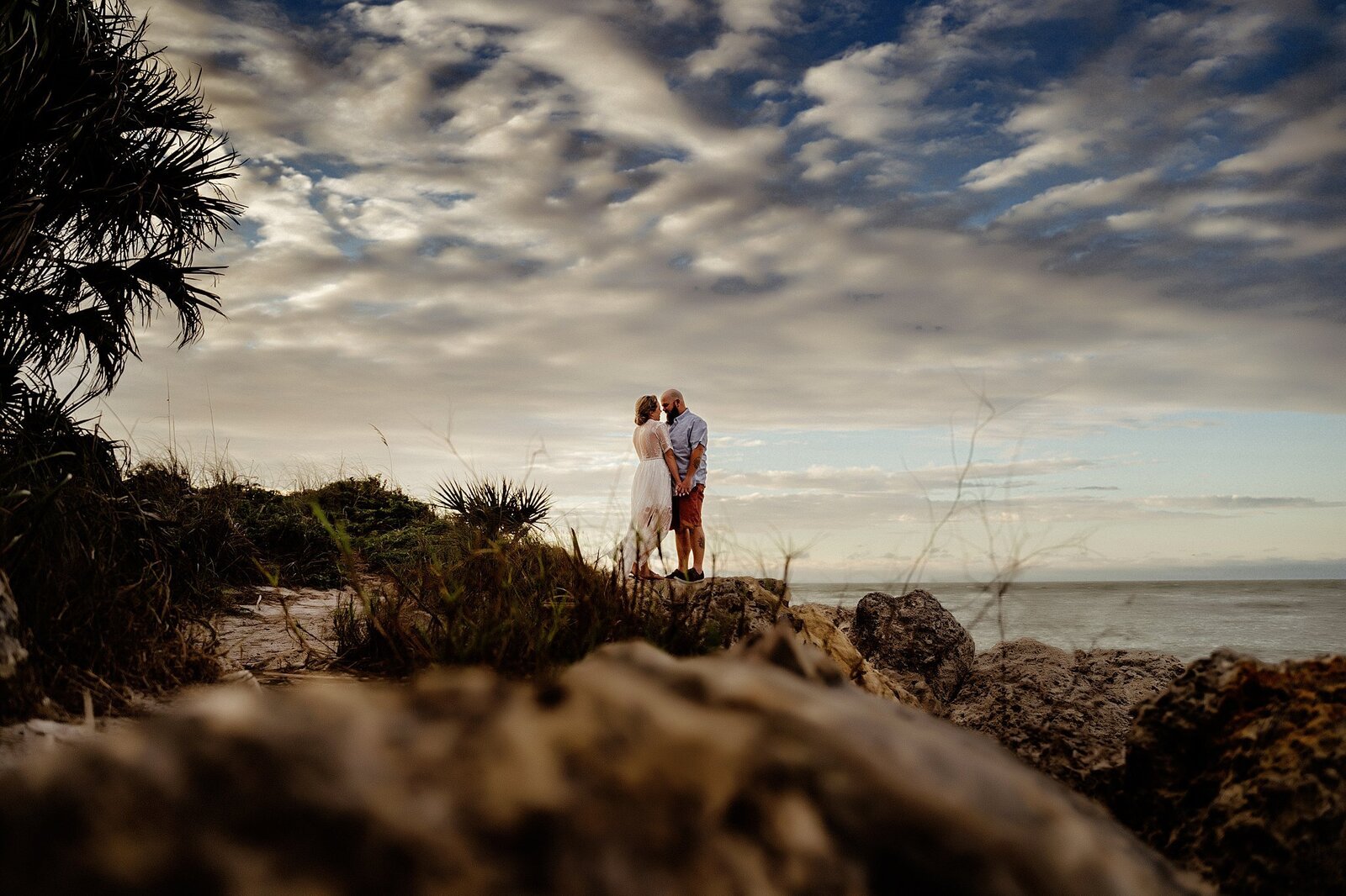 Couple in Clearwater Beach standing on rocks during sunset for engagement