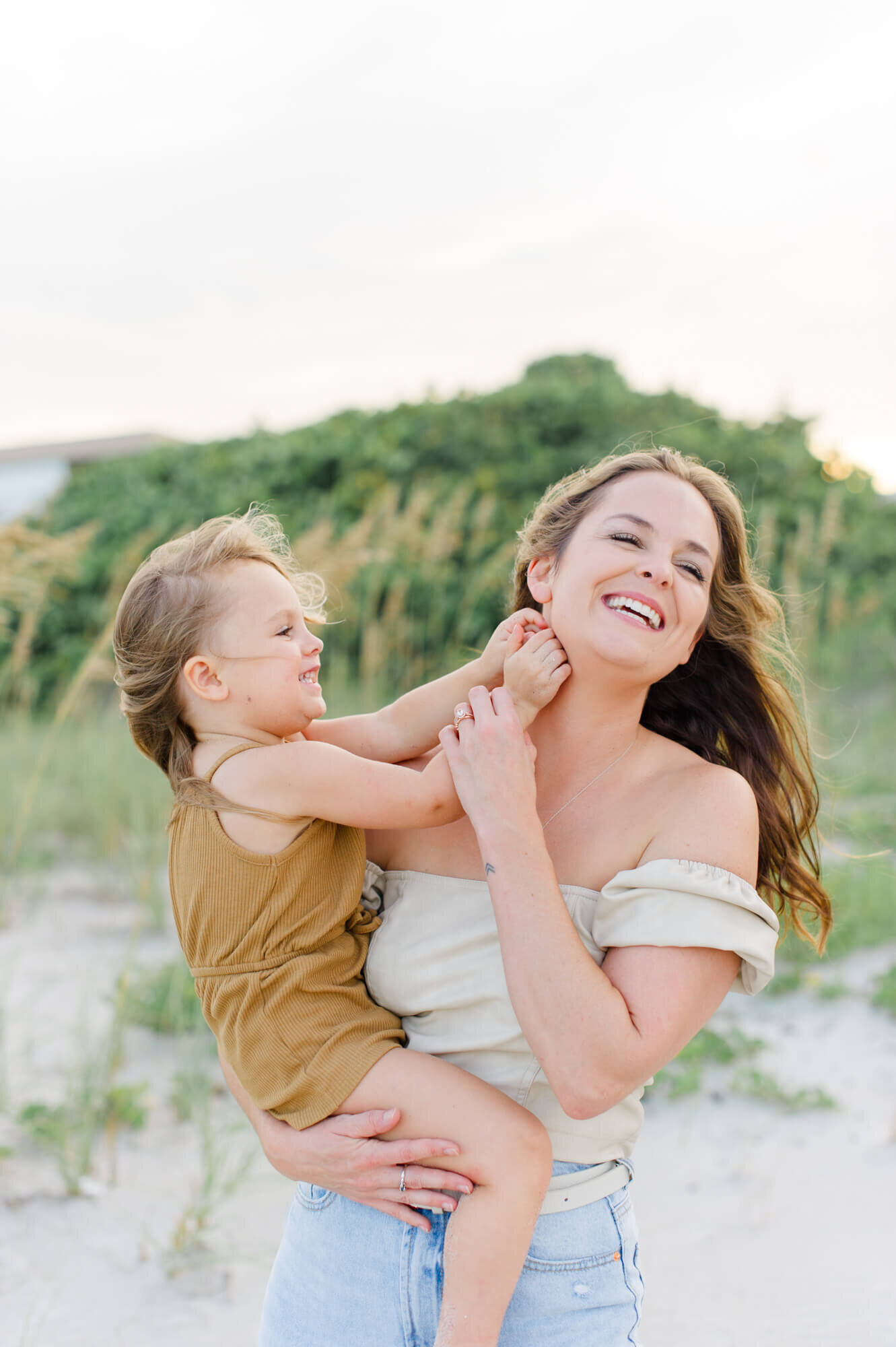 Mom holding daughter while she tickles her mom during their family beach photo session during golden hour