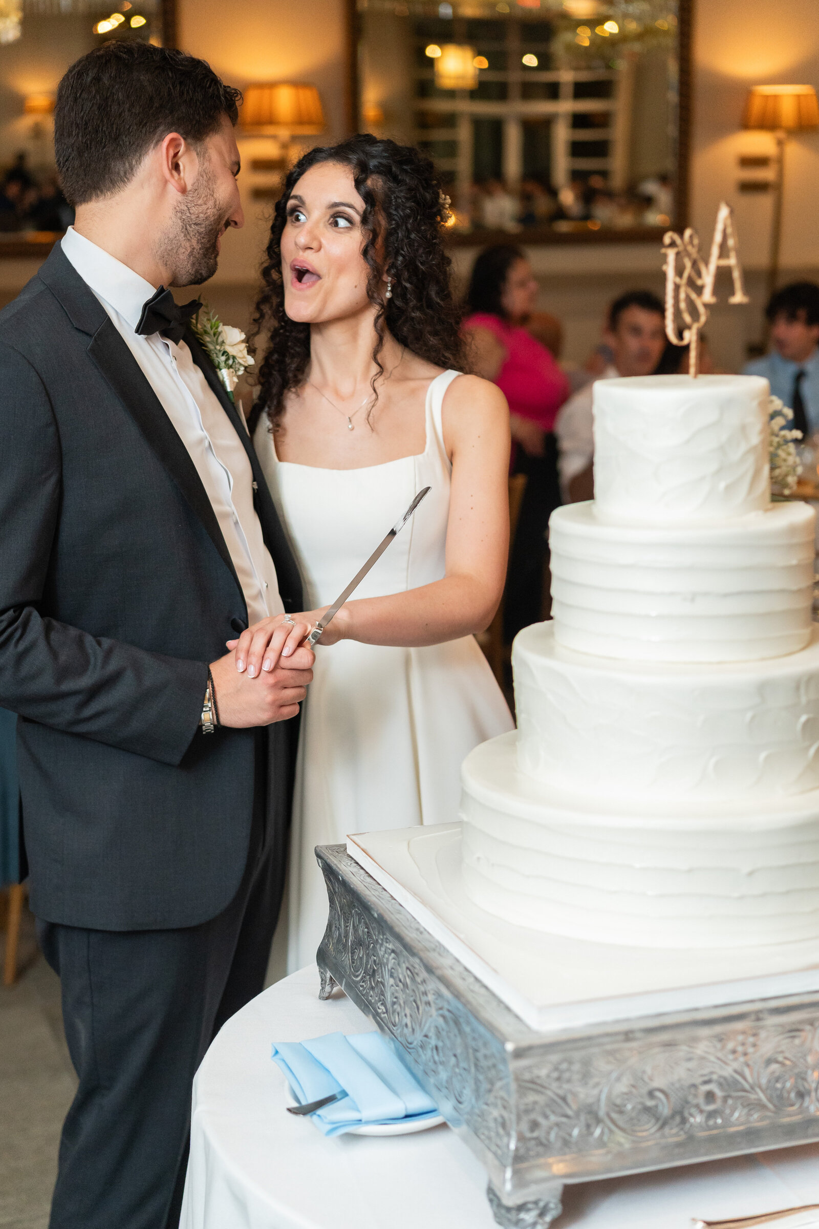 Groom holding a cake knife and a bride with a surprised expression on her face before they cut the wedding cake