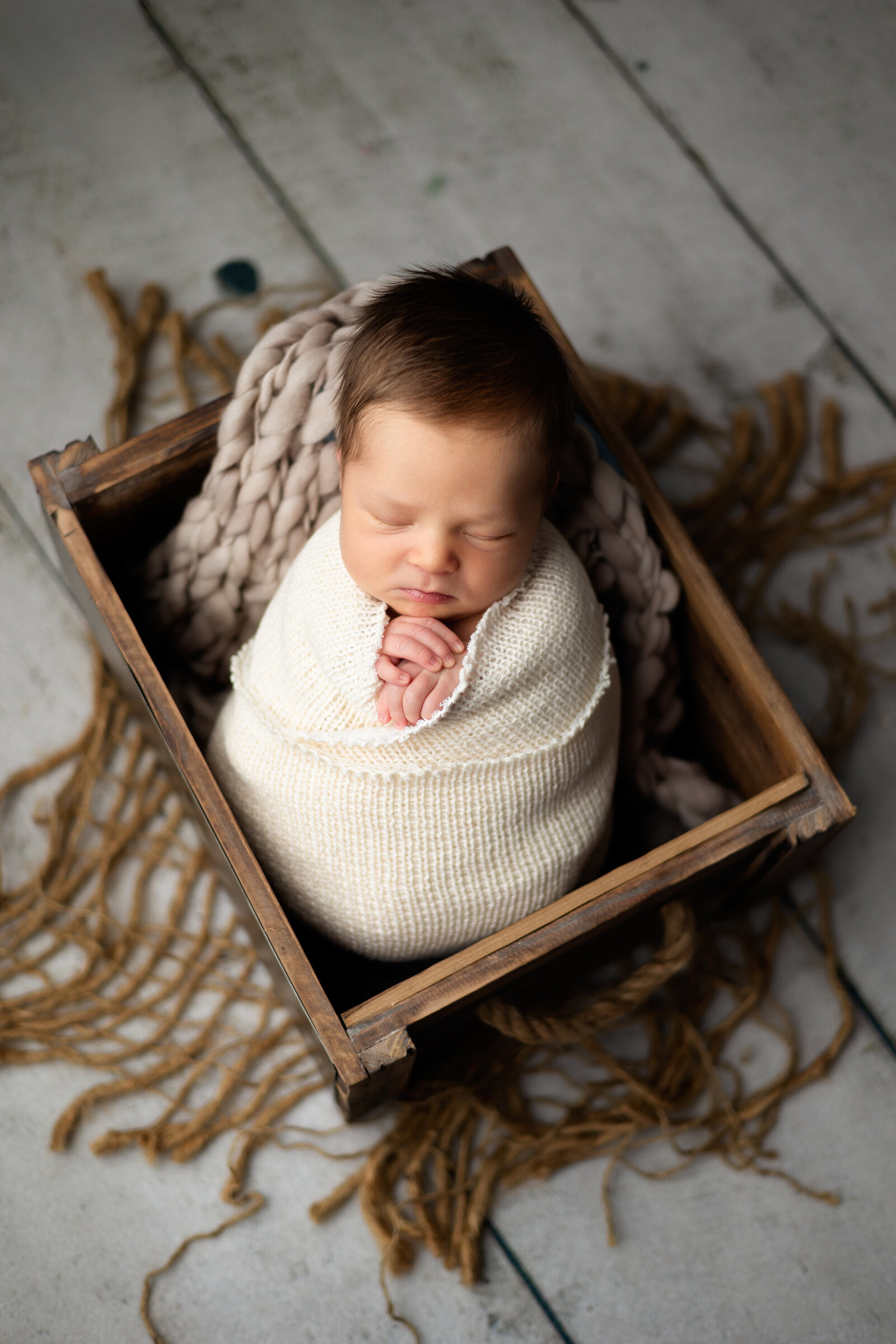 Newborn boy swaddled in a cream wrap and posed in a wooden crate