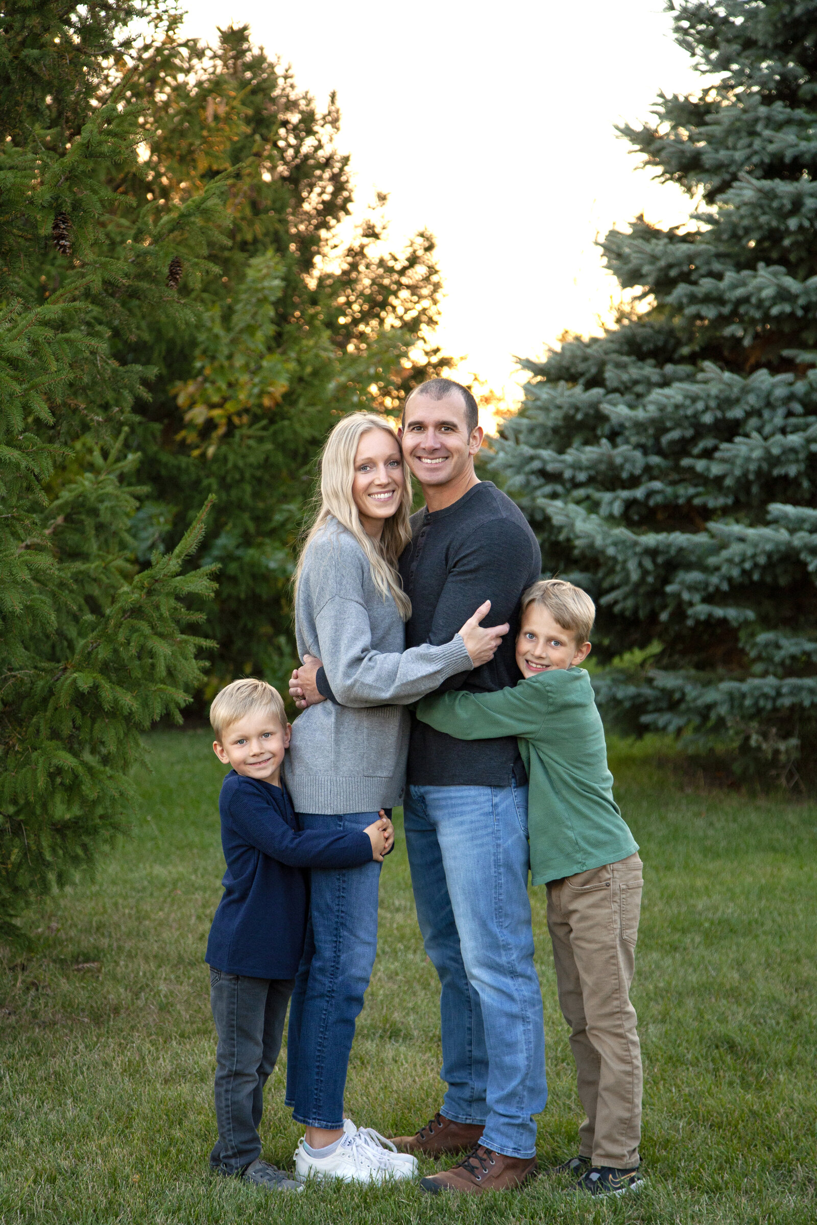 Couple hugs cheek to cheek as two sons hug their backs. 