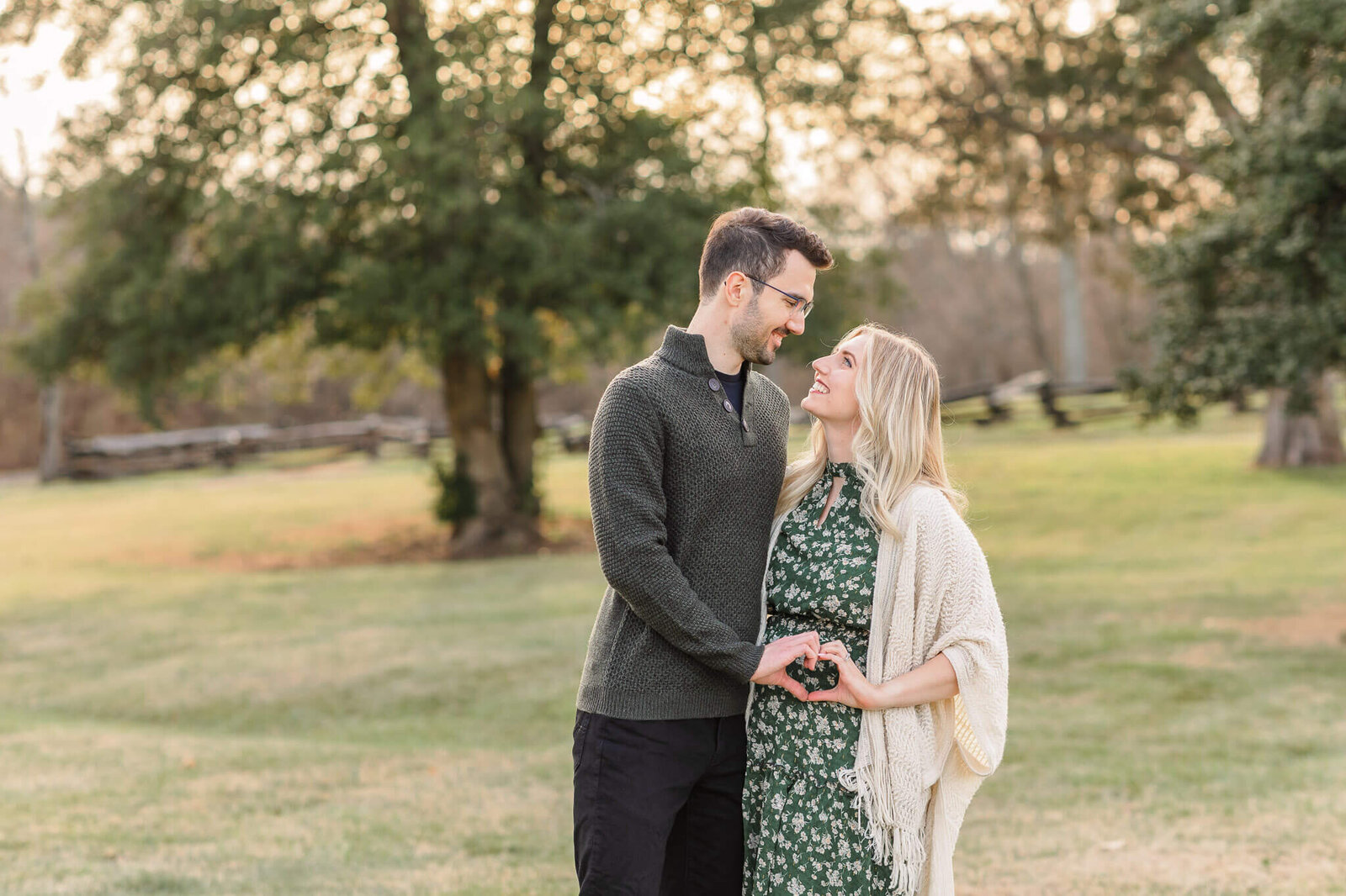 An expecting couple making a heart over mom's belly at a park at sunset.