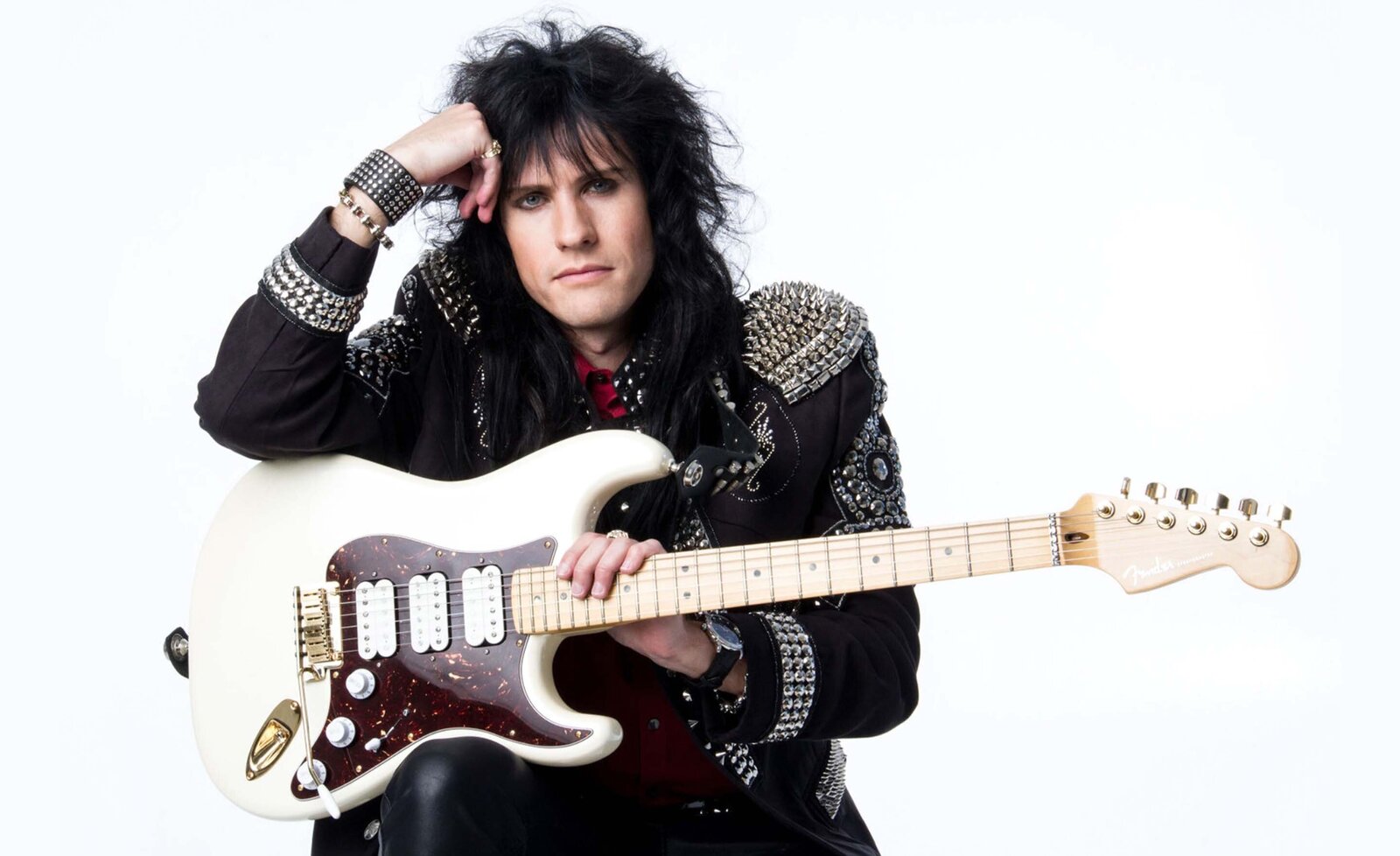 Music portrait Rocky Kramer sitting with white electric guitar against white backdrop wearing black leather jacket