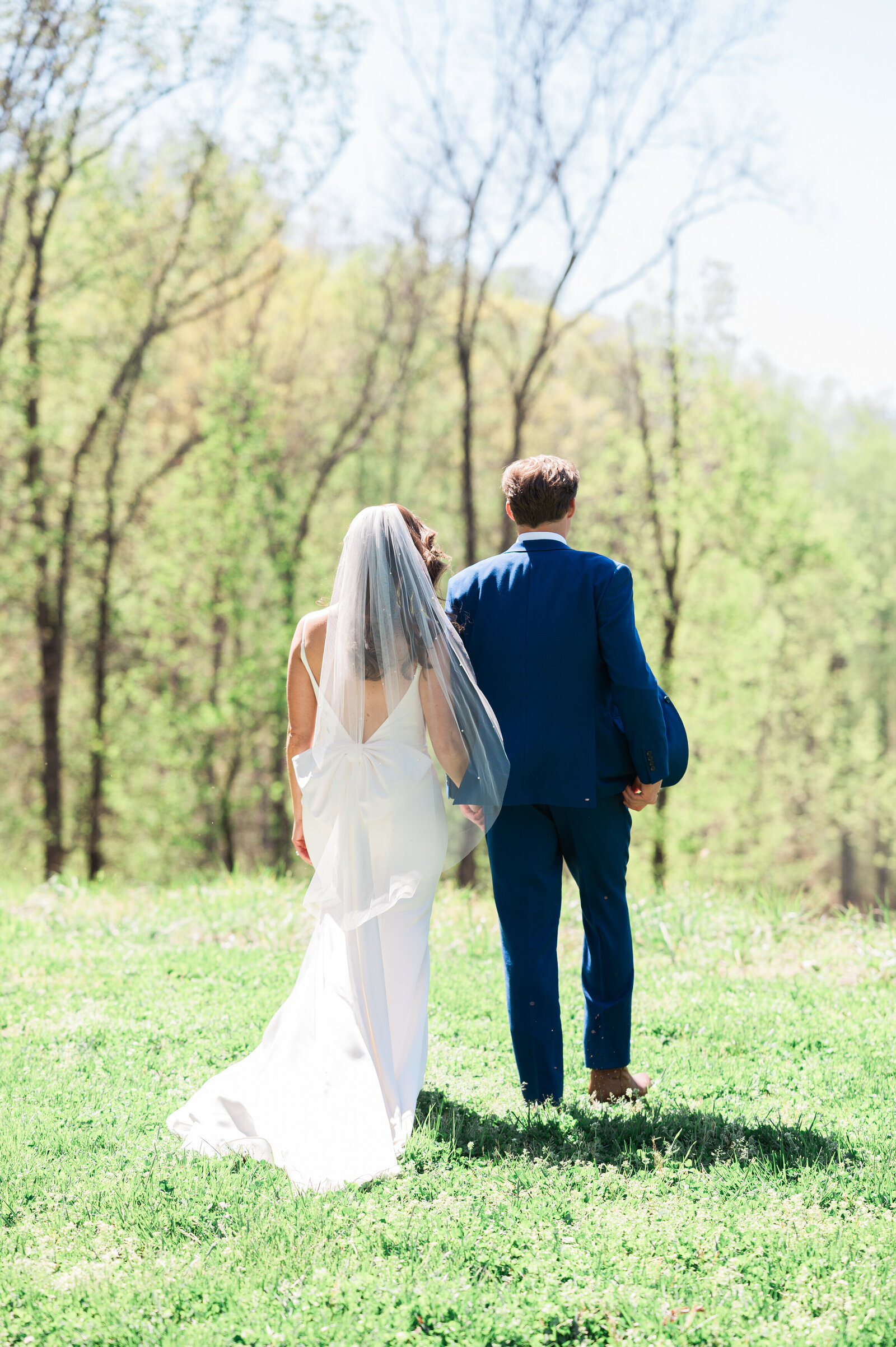 A wedding couple holding hands and walking along a grassy field