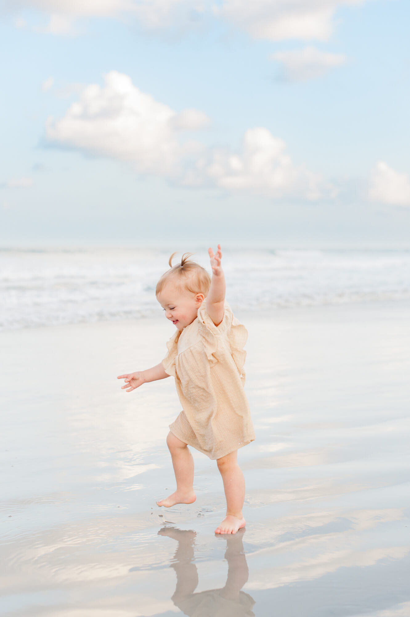 Young girl wearing adorable cream dress runs in the ocean water during their family session