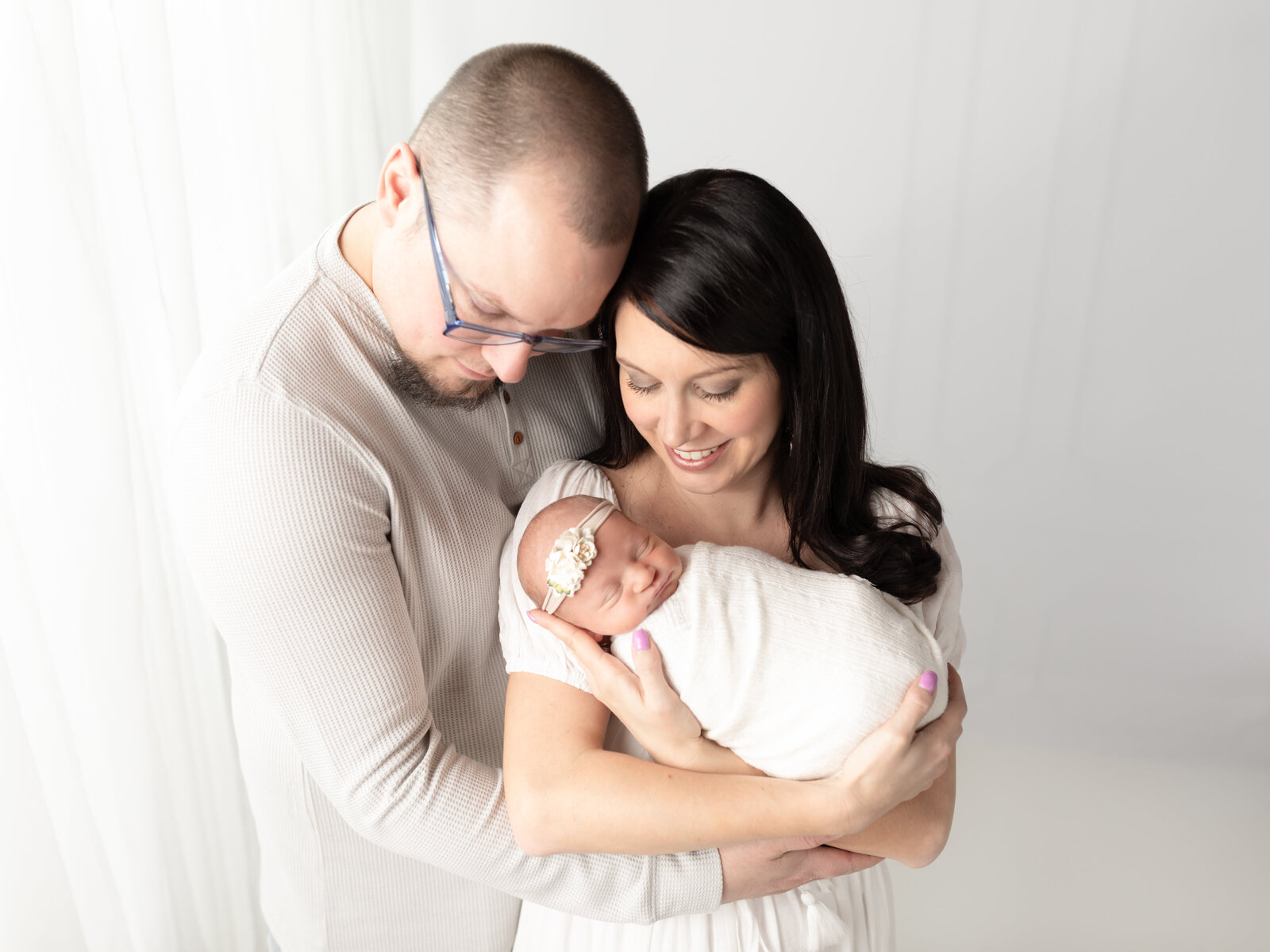 mom and dad holding newborn baby girl wrapped in white Cleveland newborn photographer