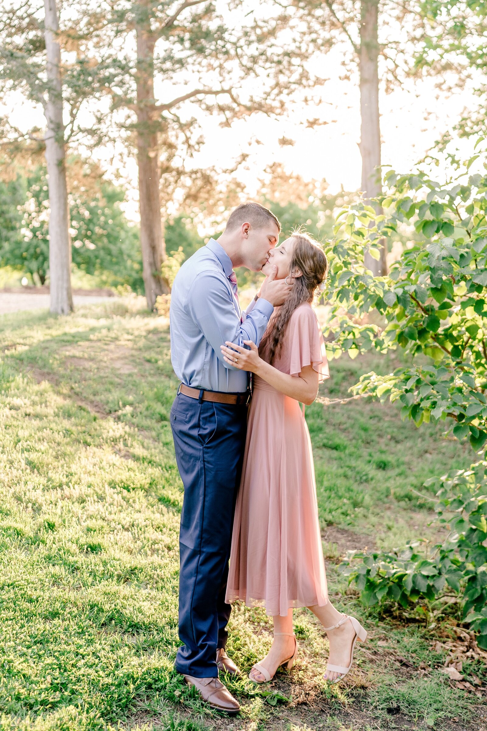 An engaged couple shares a kiss in golden hour light during their engagement session at Green Spring Gardens in Northern Virginia