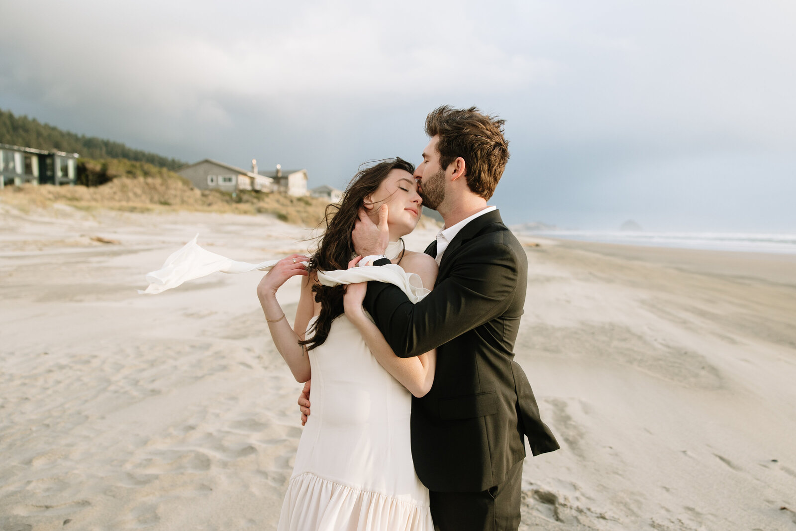 A groom kisses his bride on a windswept beach in Nova Scotia after eloping. 