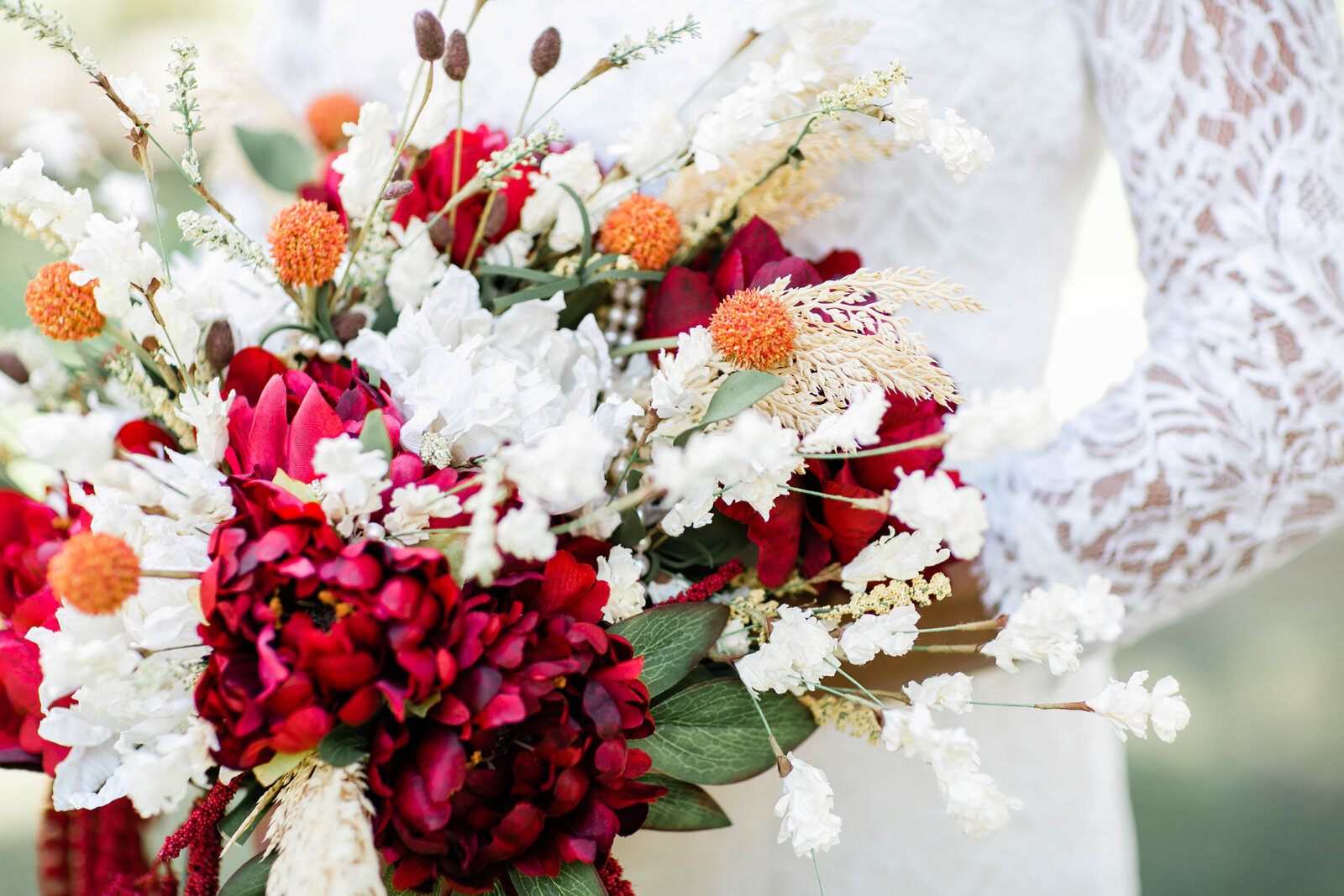 Bride holding wedding bouquet with red, white, and orange flowers and greenery