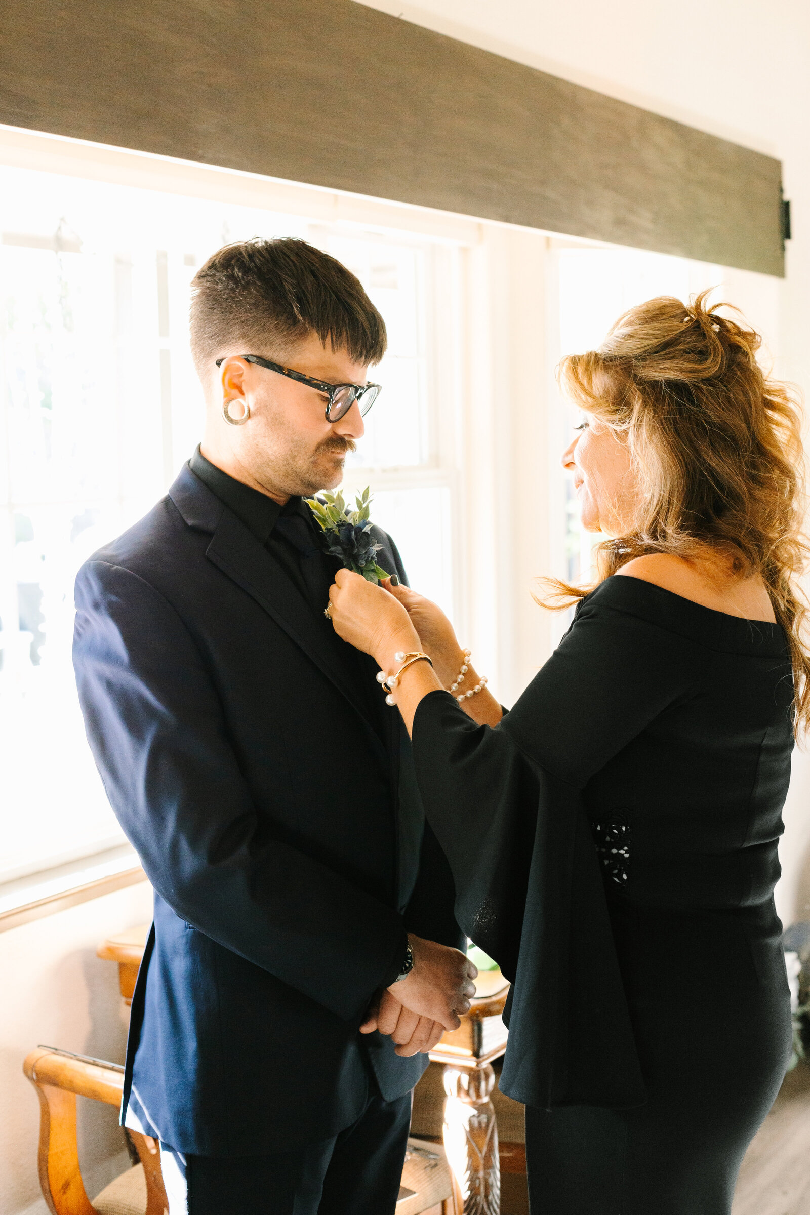 The mother of the groom puts on his boutonniere.