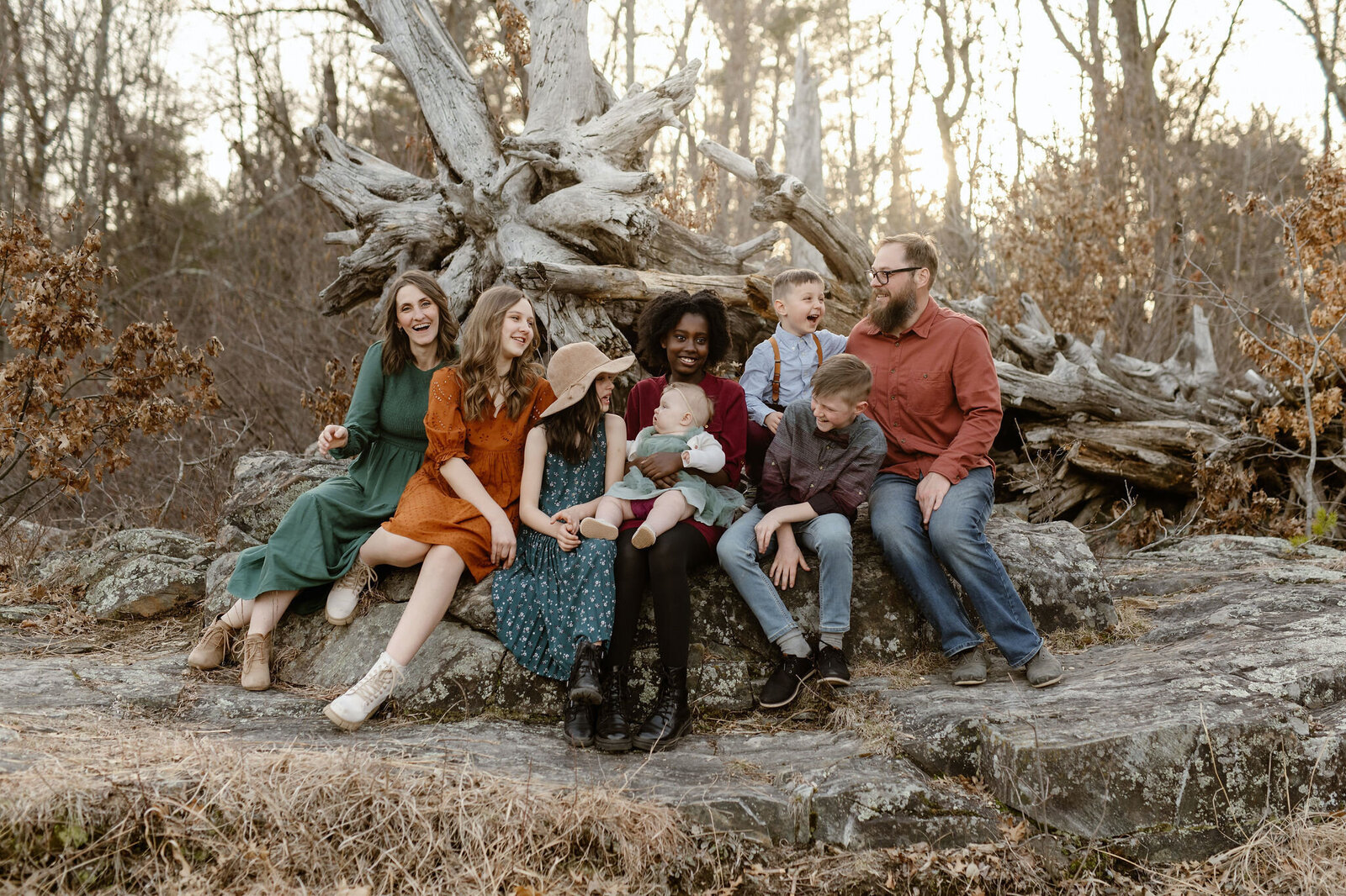 A family of eight sits on a rock, posing for their family photos.