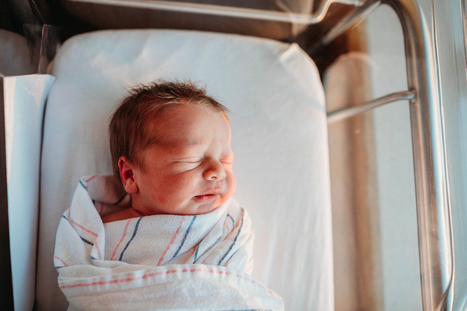 golden light falls on the face of a newborn baby lying in hospital bed