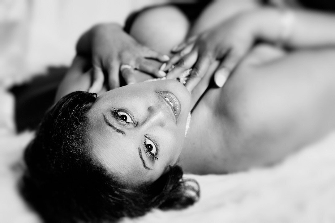A beautiful woman touching her neck while laying on a faux fur in her boudoir.
