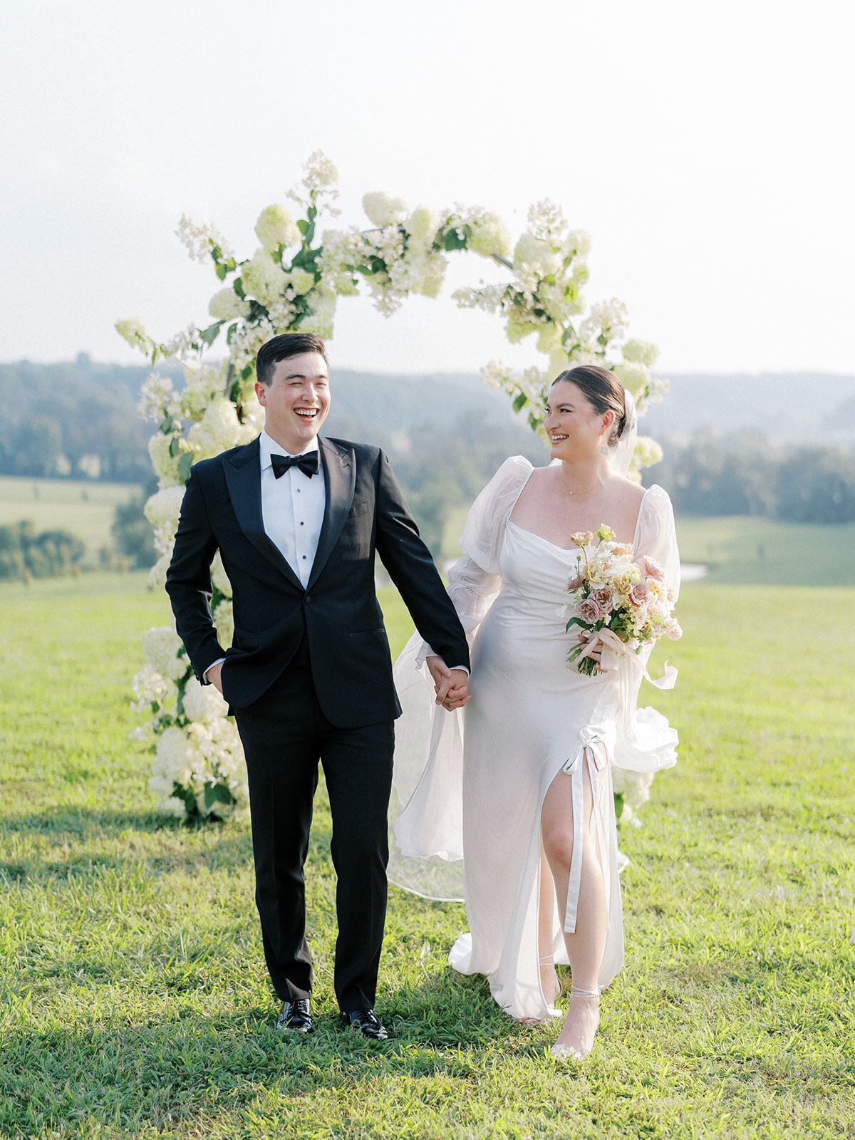 Portrait of bride and groom in front of a full coverage floral arch filled with white airy quick-fire hydrangea and limelight hydrangeas