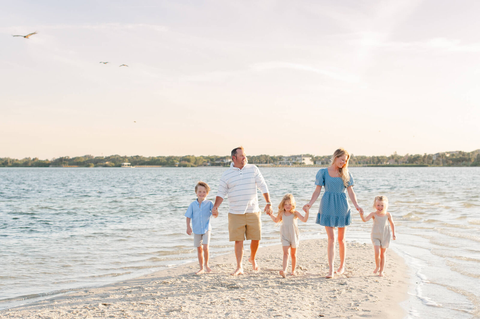 Family walking on an island holding hands with birds flying behind them