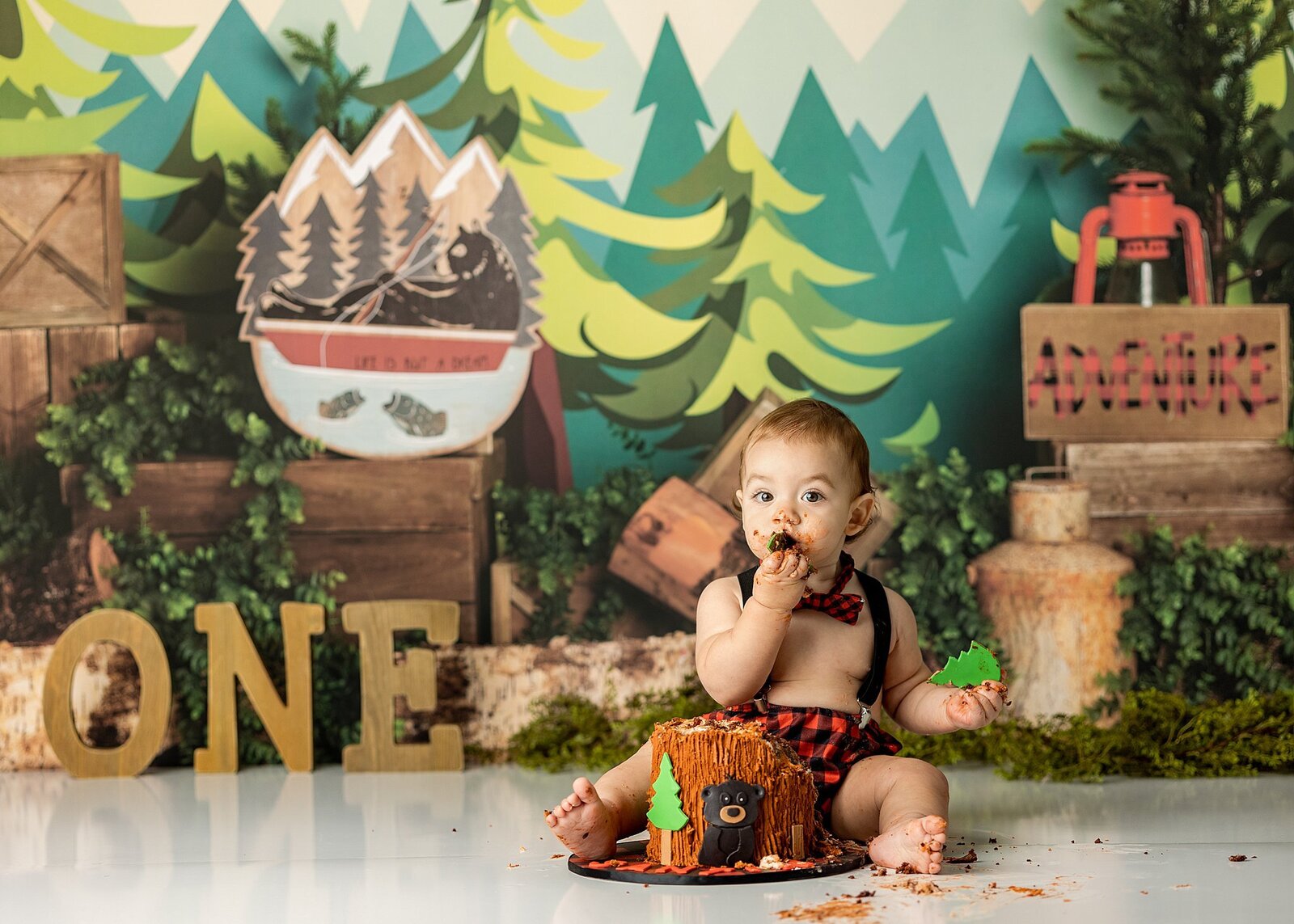 Baby boy eating a cake with a woodsy theme backdrop.