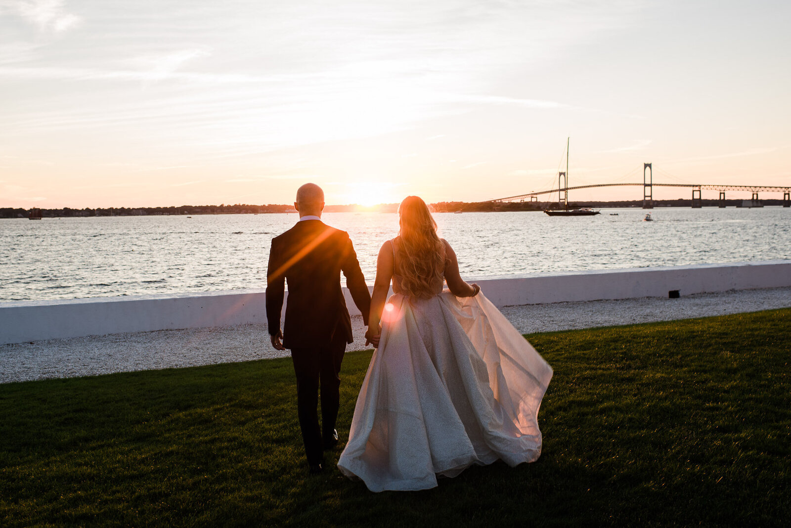 bride and groom hold hands walk to water at sunset