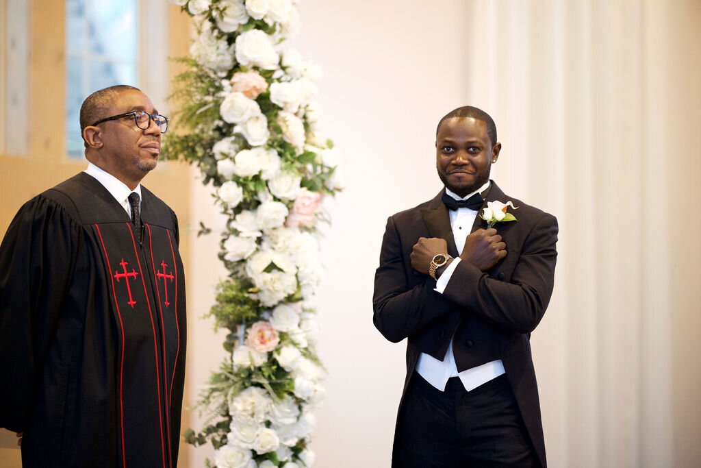 groom with his arms crossed over his chest and smiling as her looks down the aisle at the bride