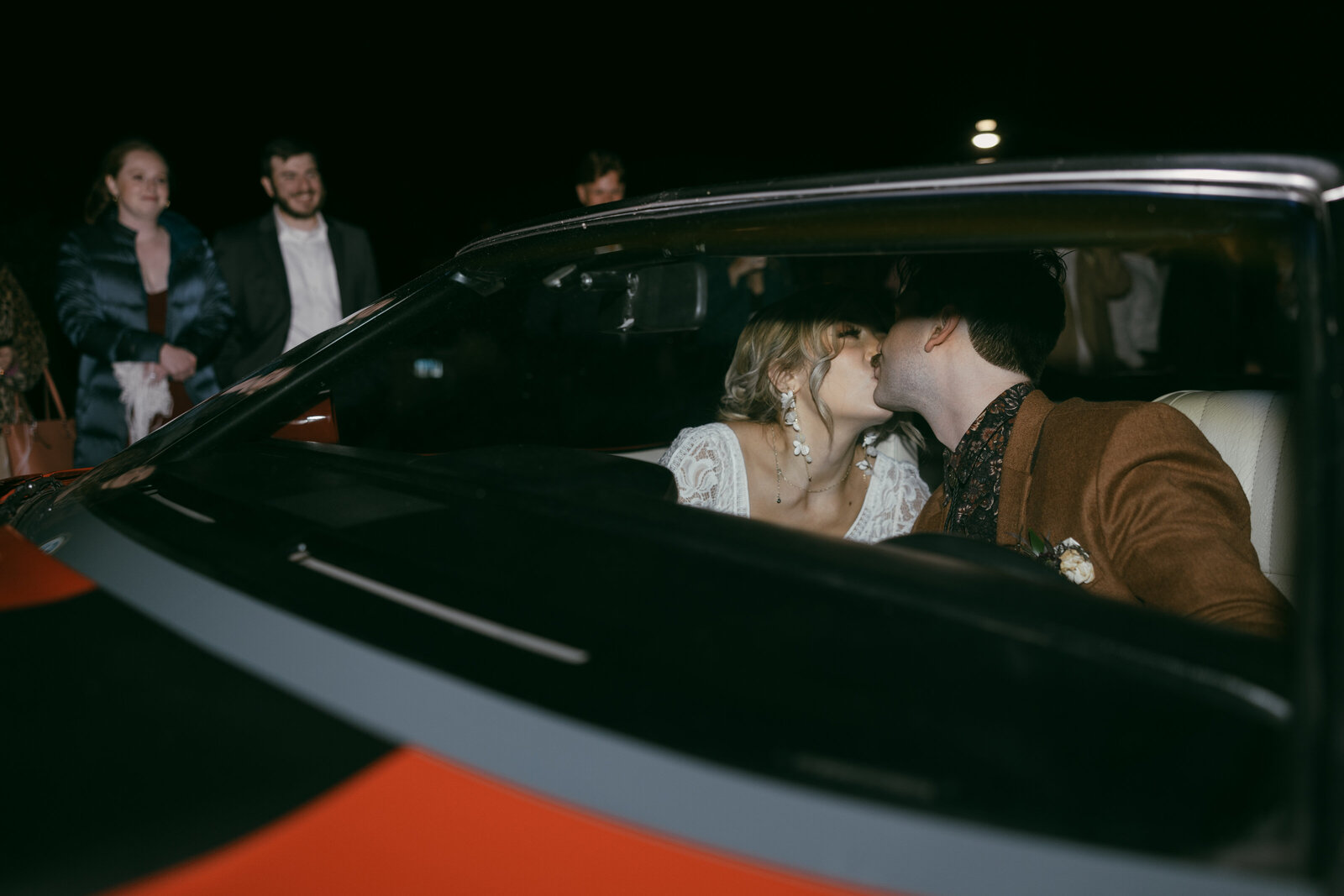 Wedding portrait, night time send off with bride and groom kissing in a classic convertible