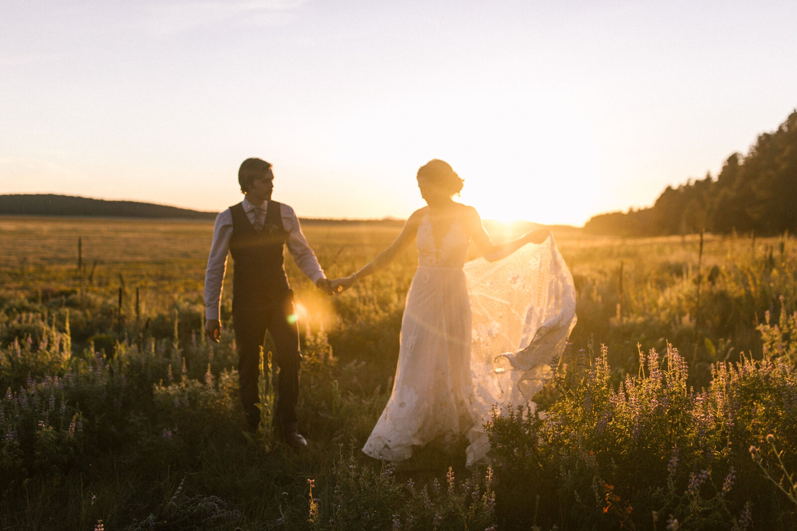 Wedding couple holding hands in field with sun shining behind
